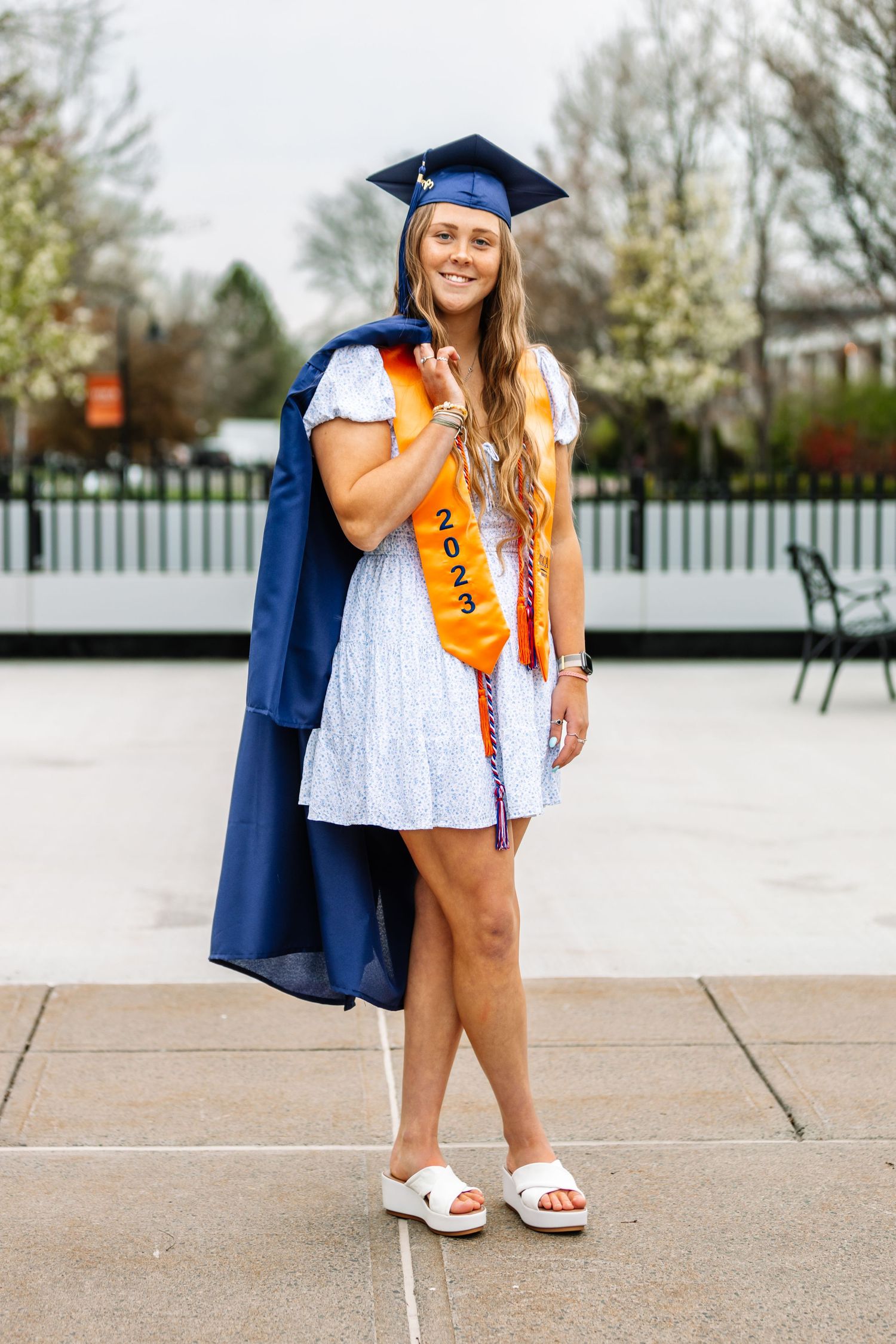 Girl wearing graduation cap holding graduation gown over her shoulder