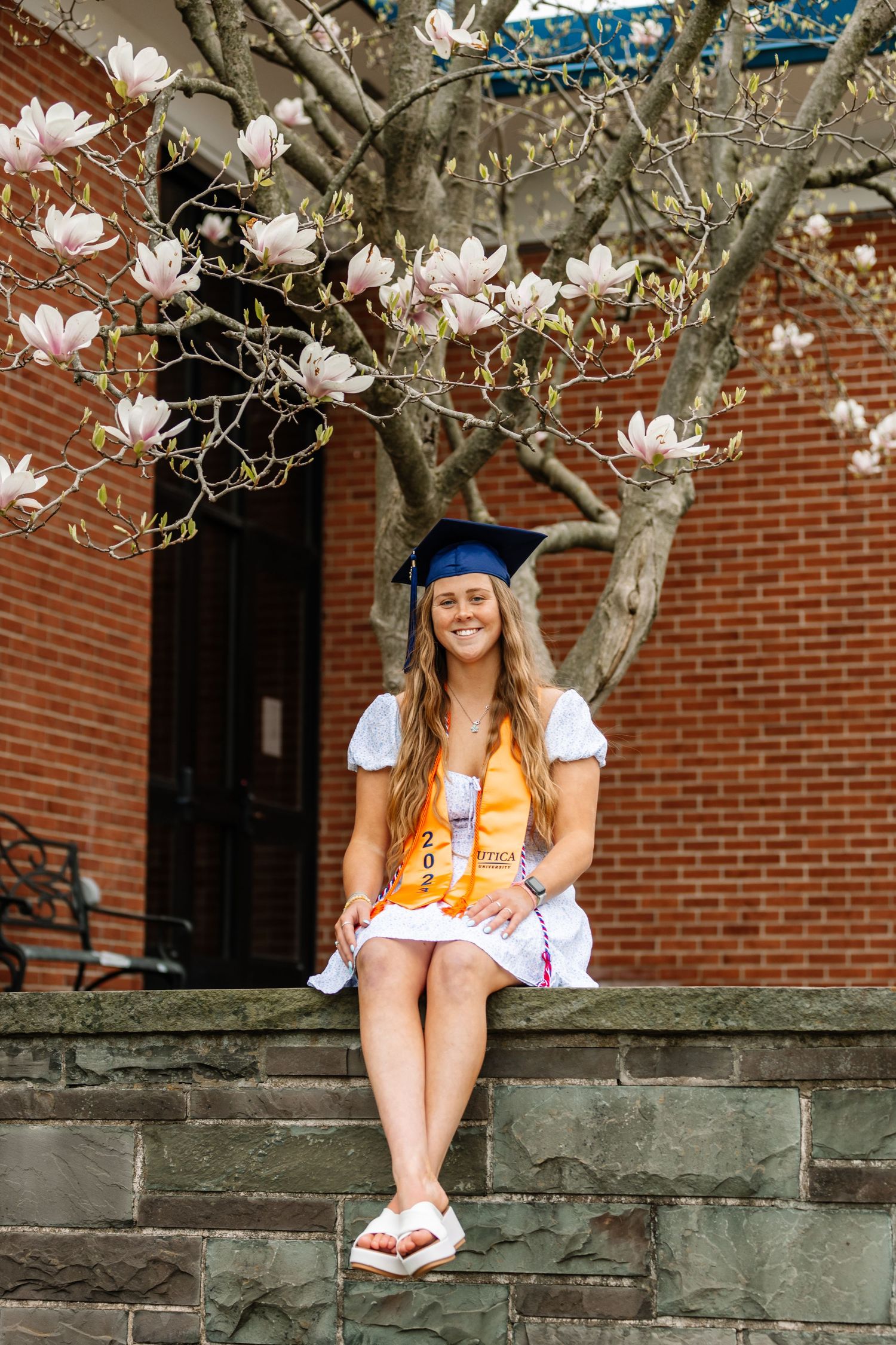 Girl wearing graduation cap sitting on rock wall