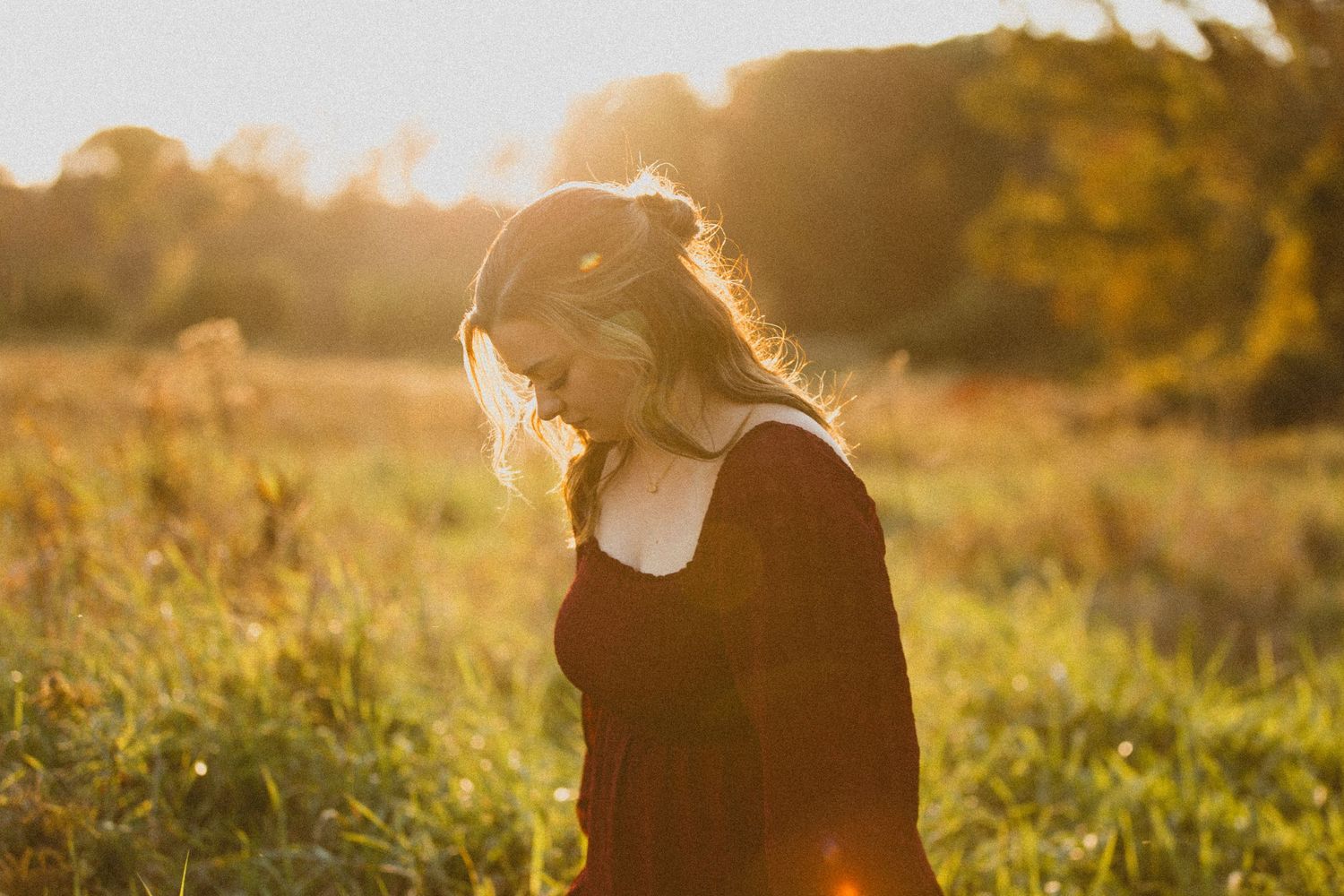 Girl wearing maroon dress posing in field in golden hour light