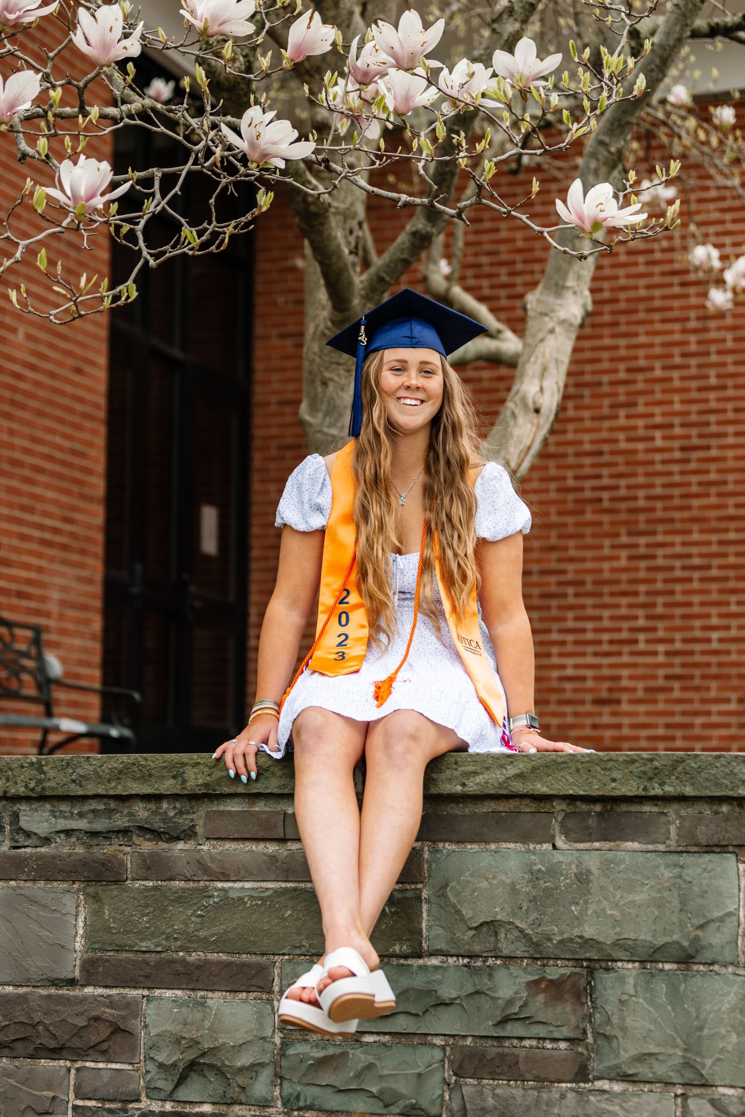 Girl wearing graduation cap sitting on rock wall