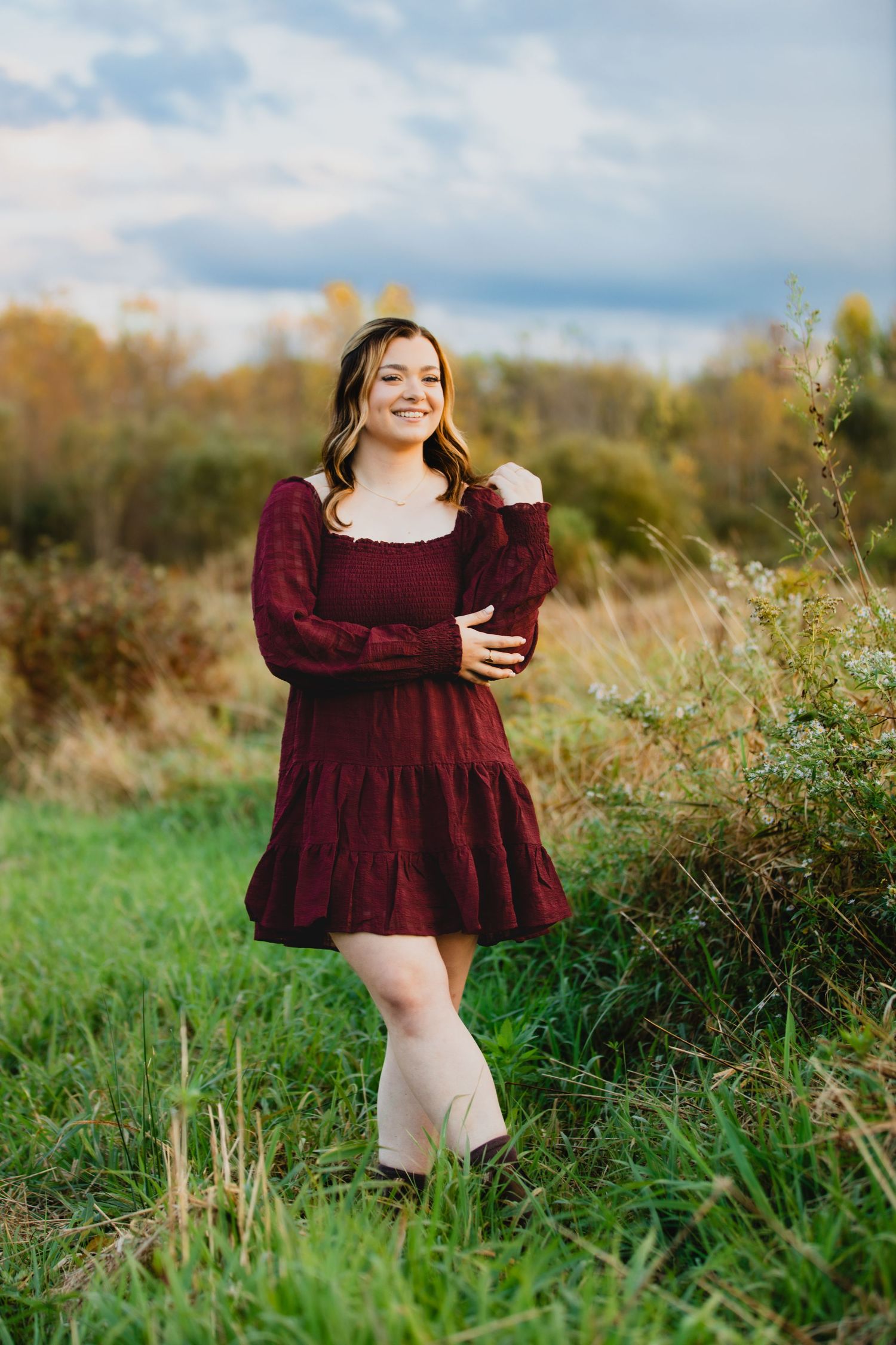 Girl wearing maroon dress posing in field in golden hour light
