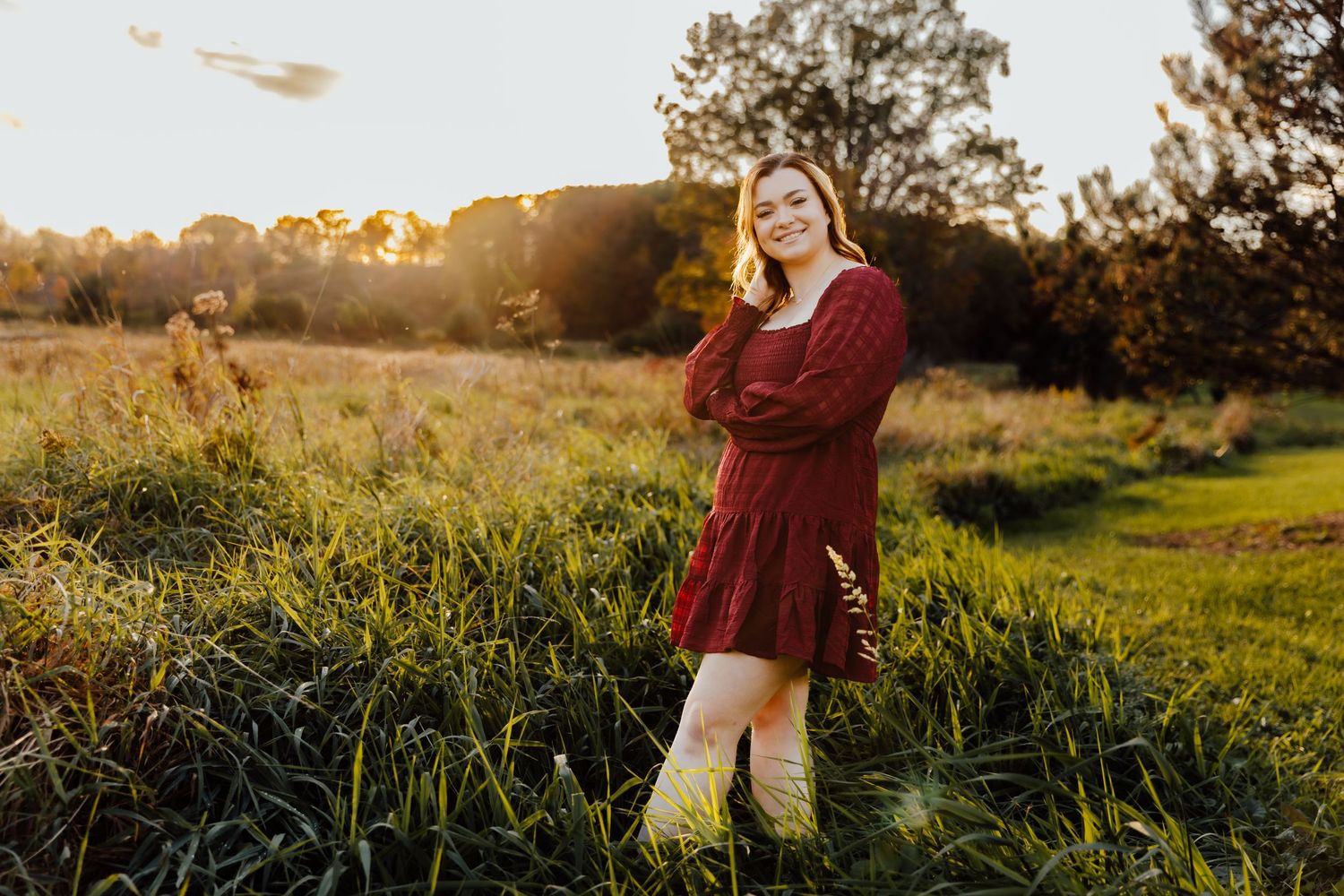 Girl wearing maroon dress posing in field in golden hour light