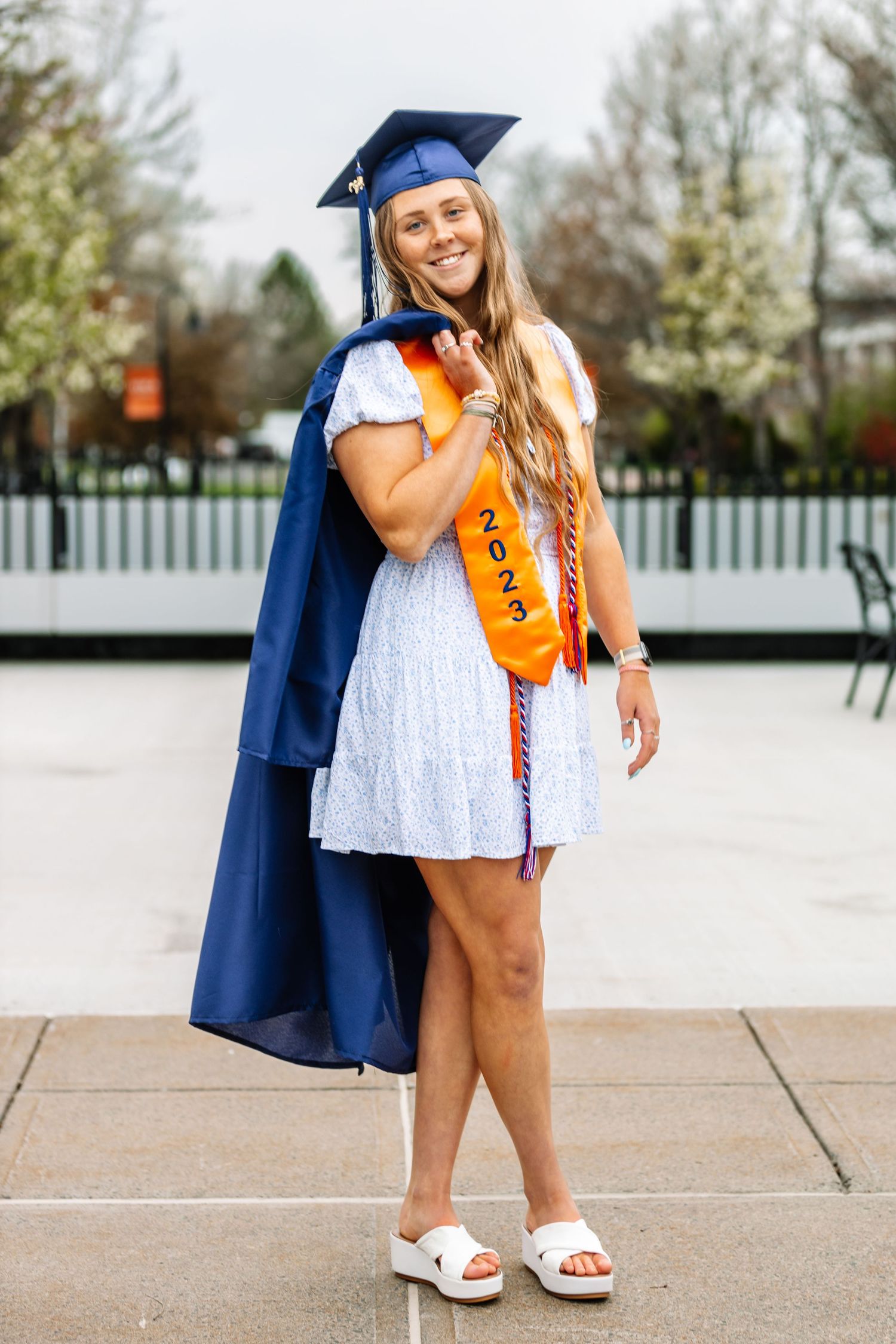 Girl wearing graduation cap holding graduation gown over her shoulder
