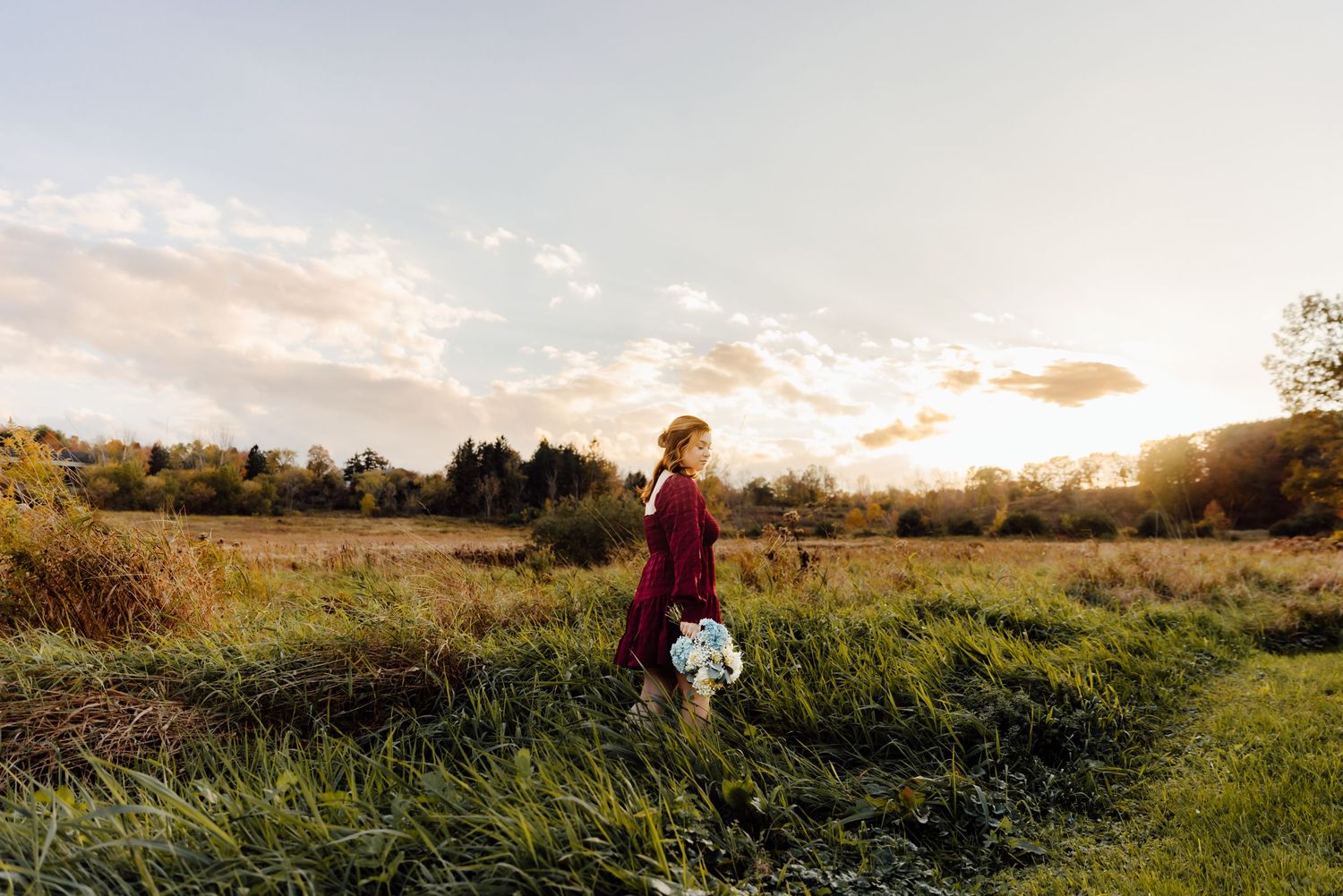Girl wearing maroon dress posing in field in golden hour light
