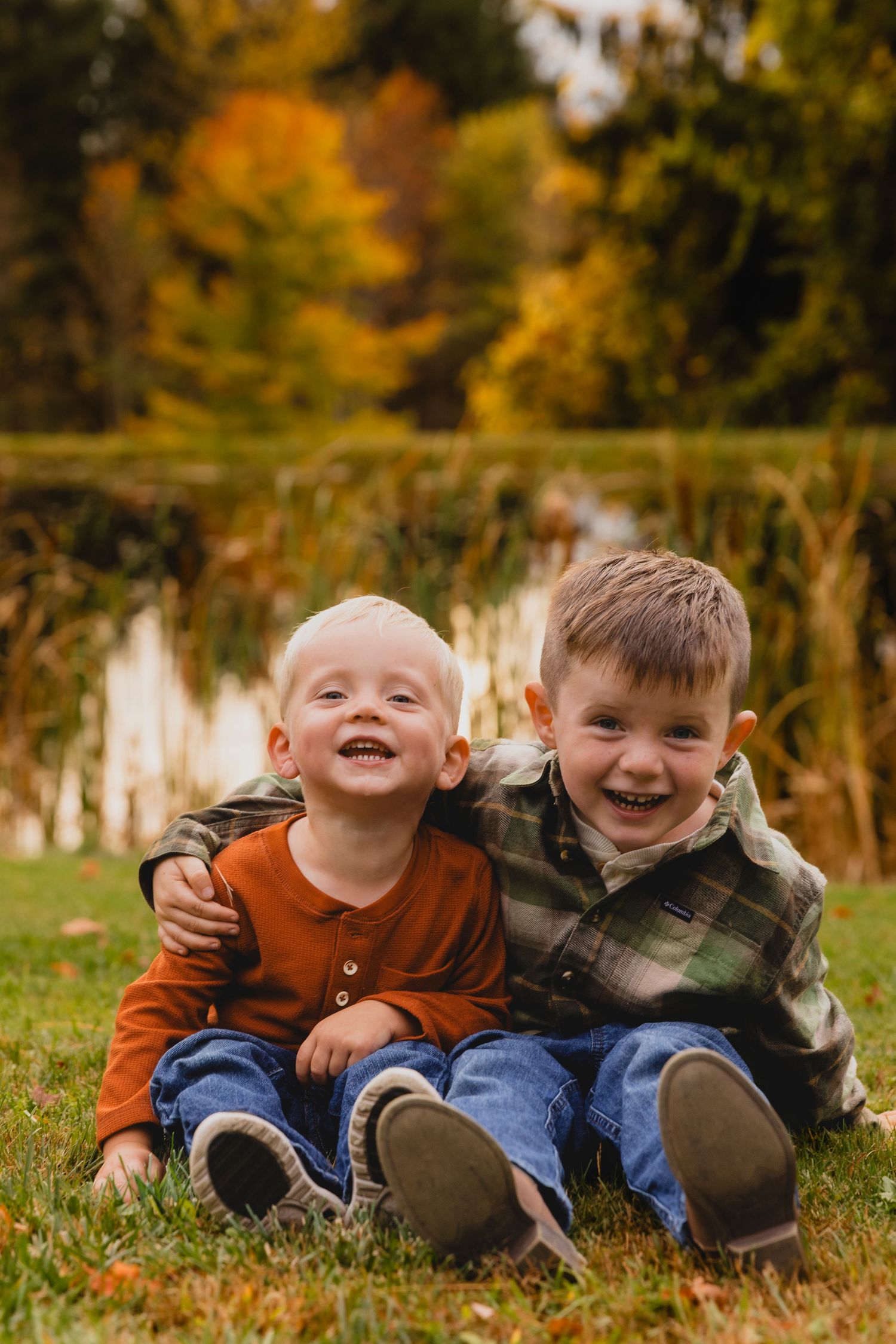 Two brothers sitting in grass with pond behind them