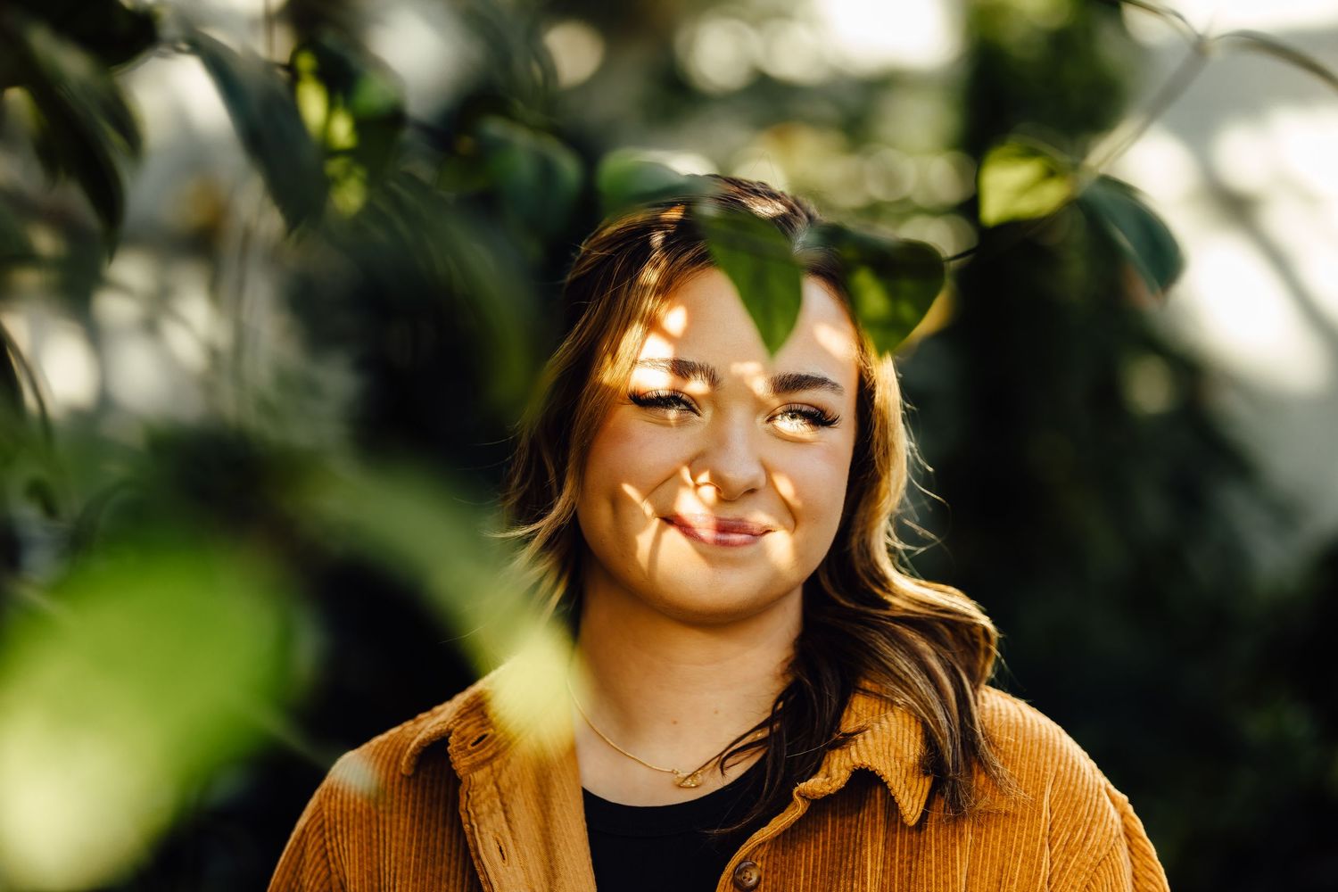 Girl in greenhouse with plants in foreground and speckled light on her face