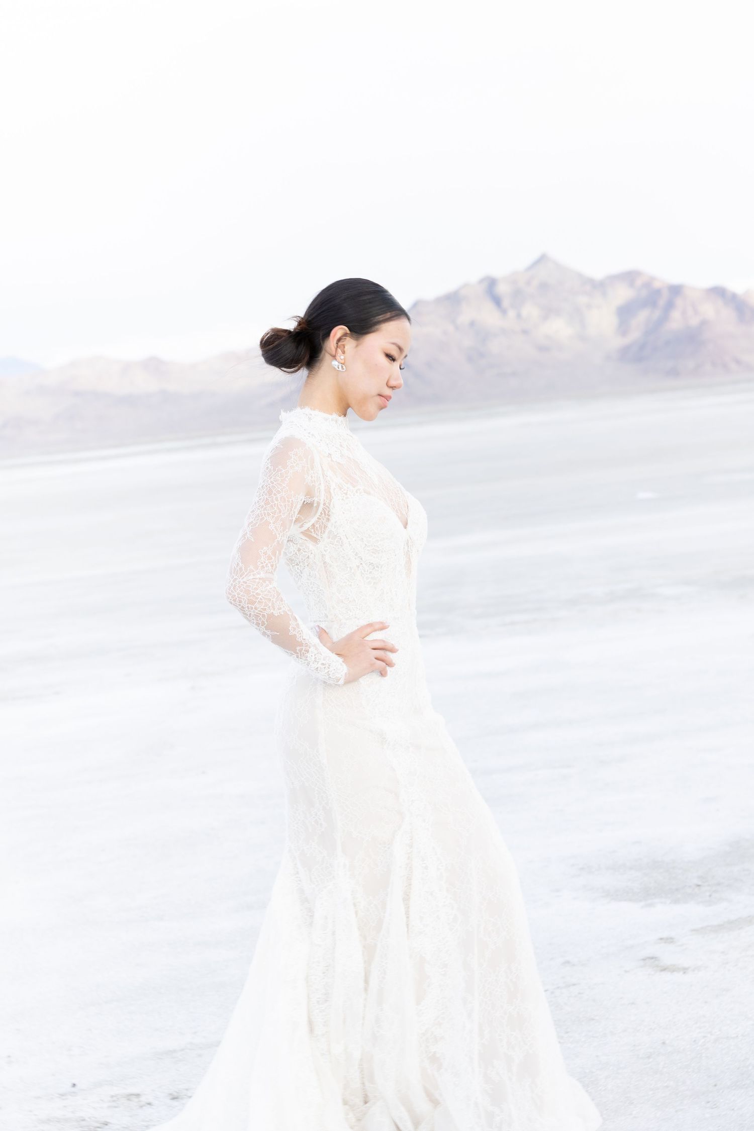 Ethereal bridal portrait in a white lace gown against a stark desert landscape.