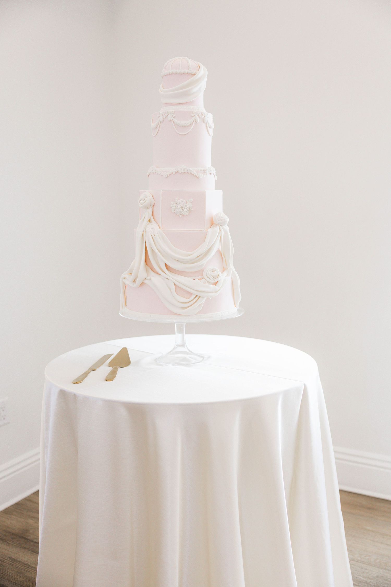 Elegant five-tier white wedding cake with draped fondant details on a white tablecloth pedestal table.
