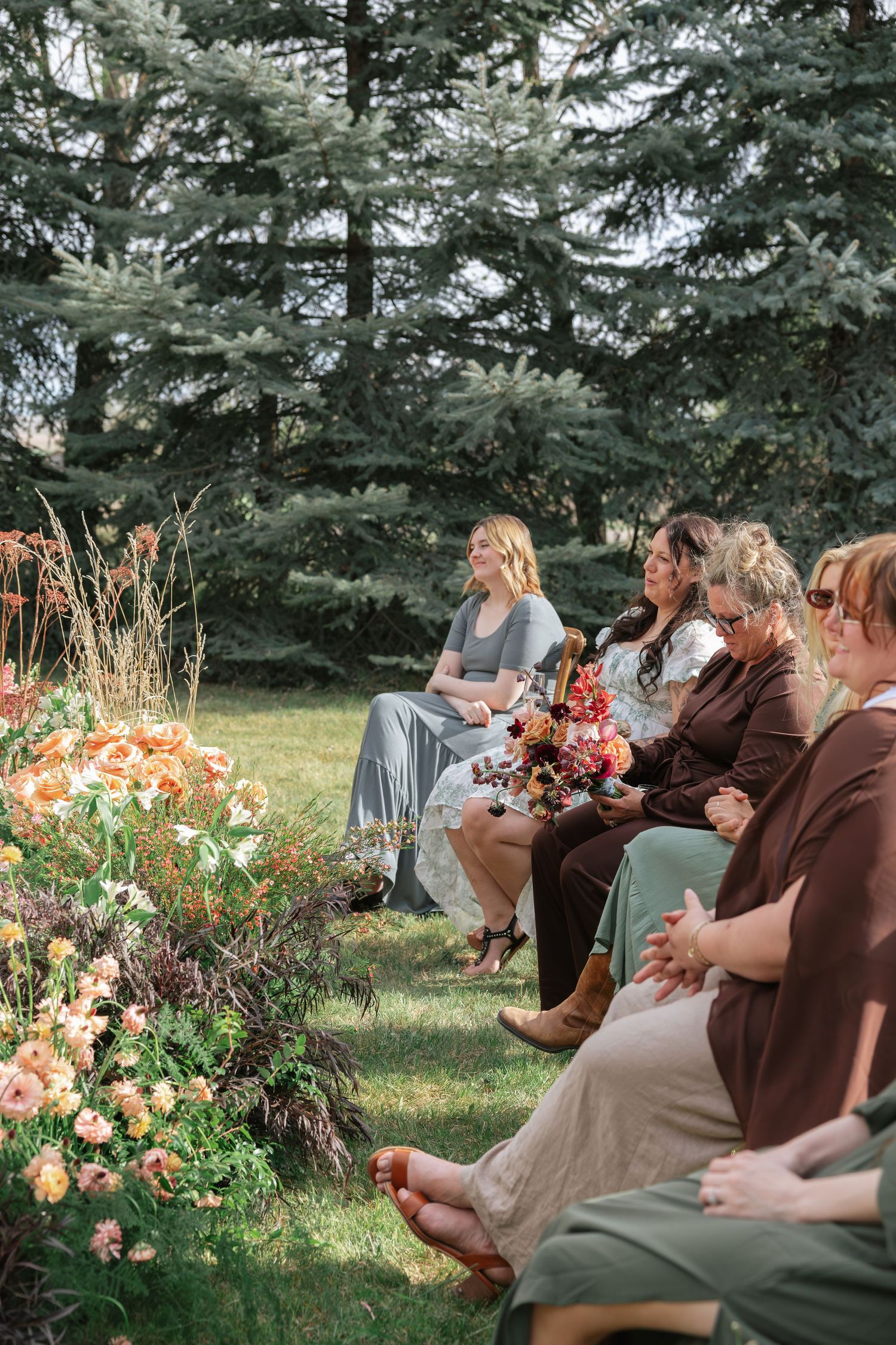 Wedding guests seated outdoors along floral-lined aisle with vibrant peach and burgundy flower arrangements.