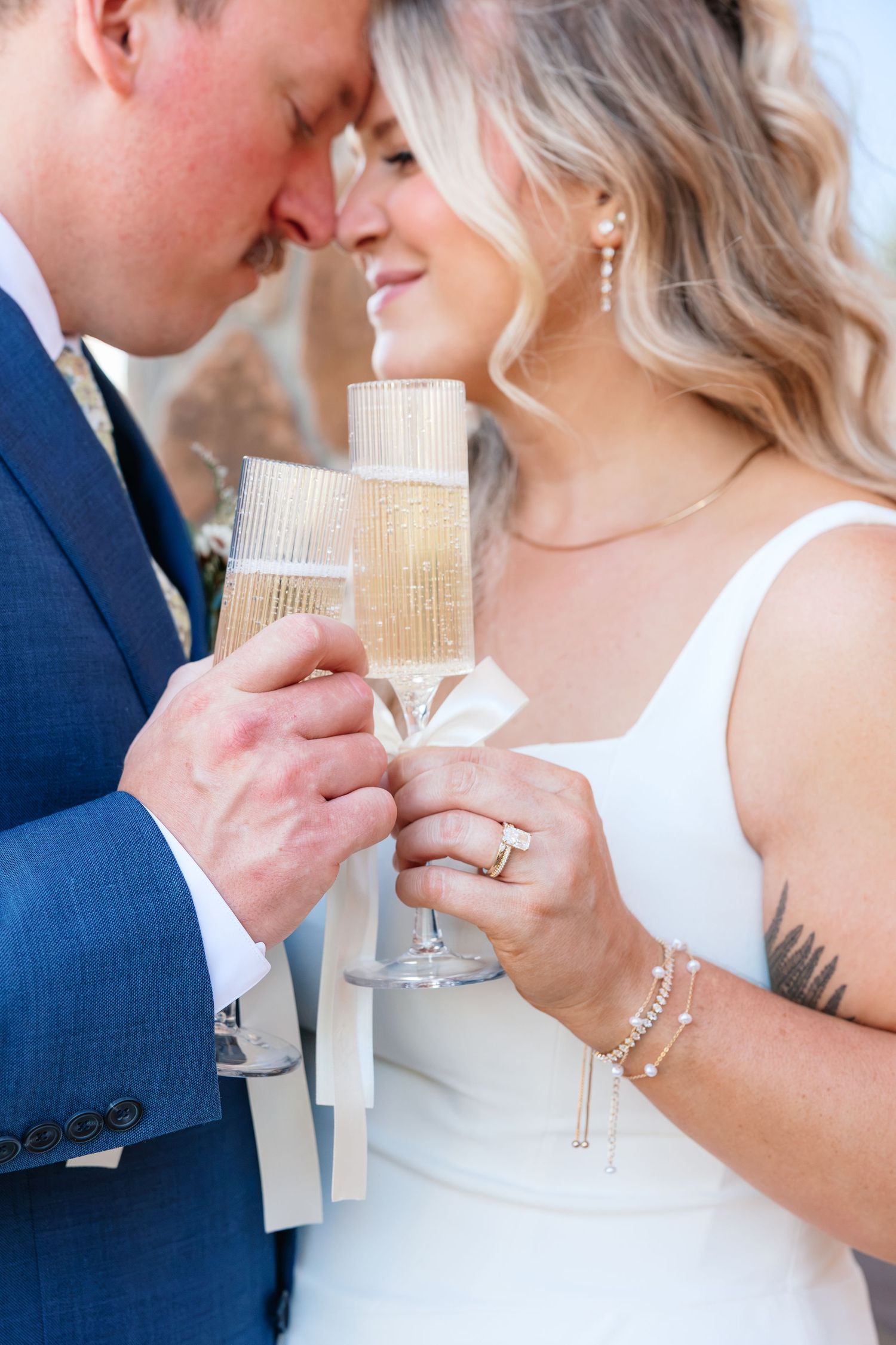 Bride and groom touching foreheads and clinking champagne flutes in a romantic wedding toast celebration.
