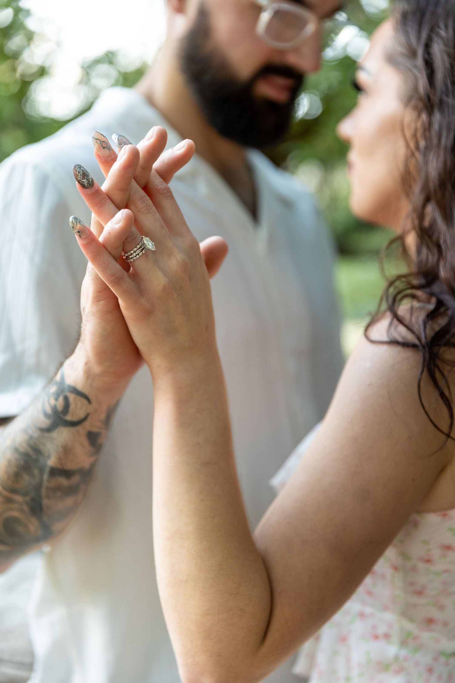 Couple holding hands outdoors, woman wearing engagement ring and nail art, man with beard and tattoos.