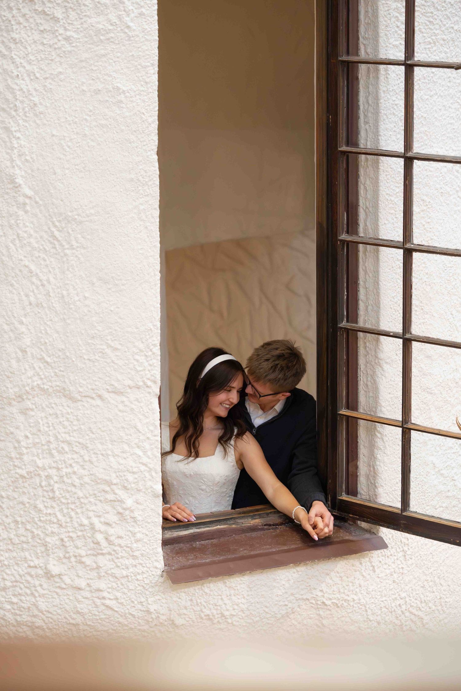 A bride and groom share a romantic moment together while leaning out of a rustic window with iron bars.