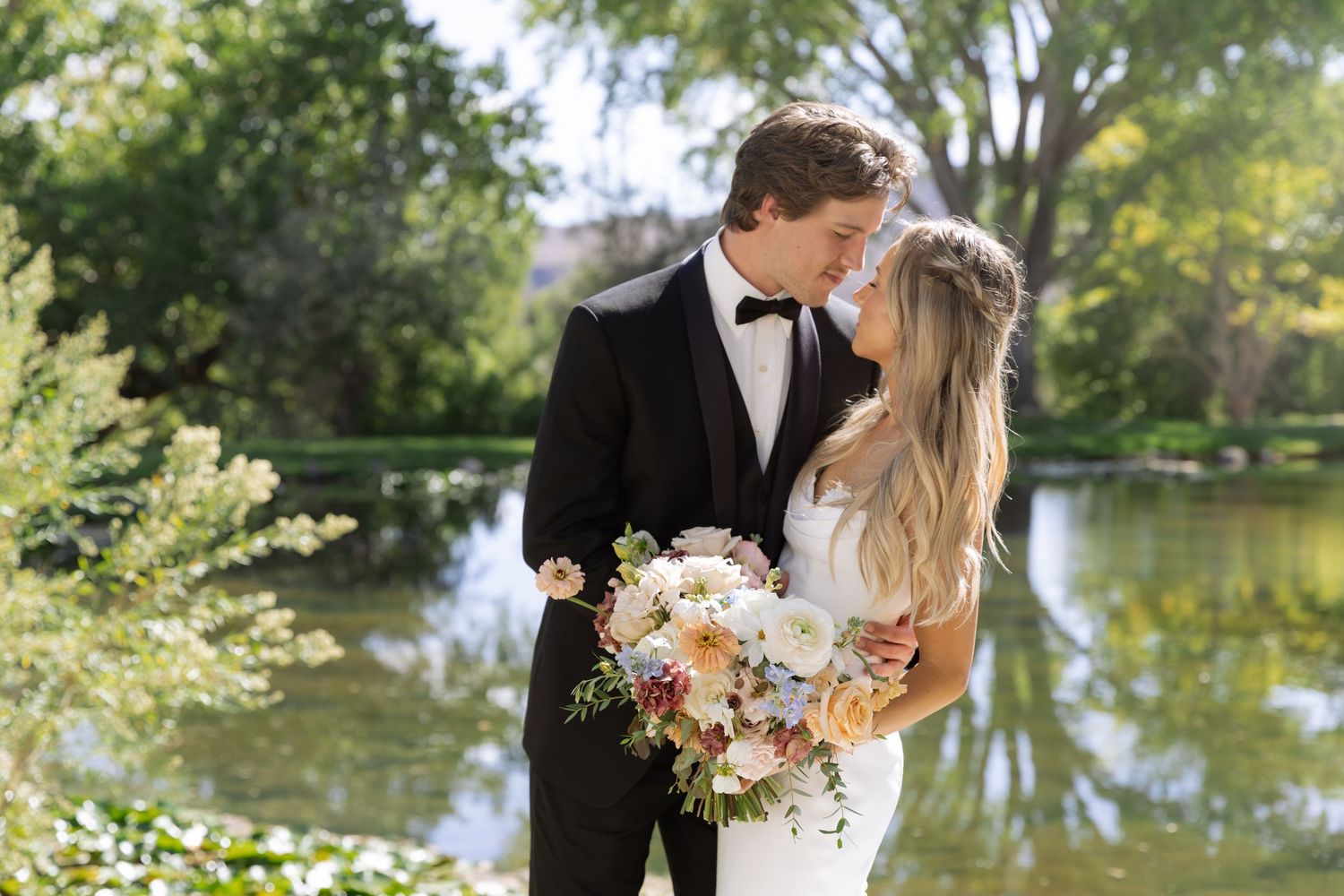 Couple shares intimate wedding photos by a tranquil pond with natural greenery.