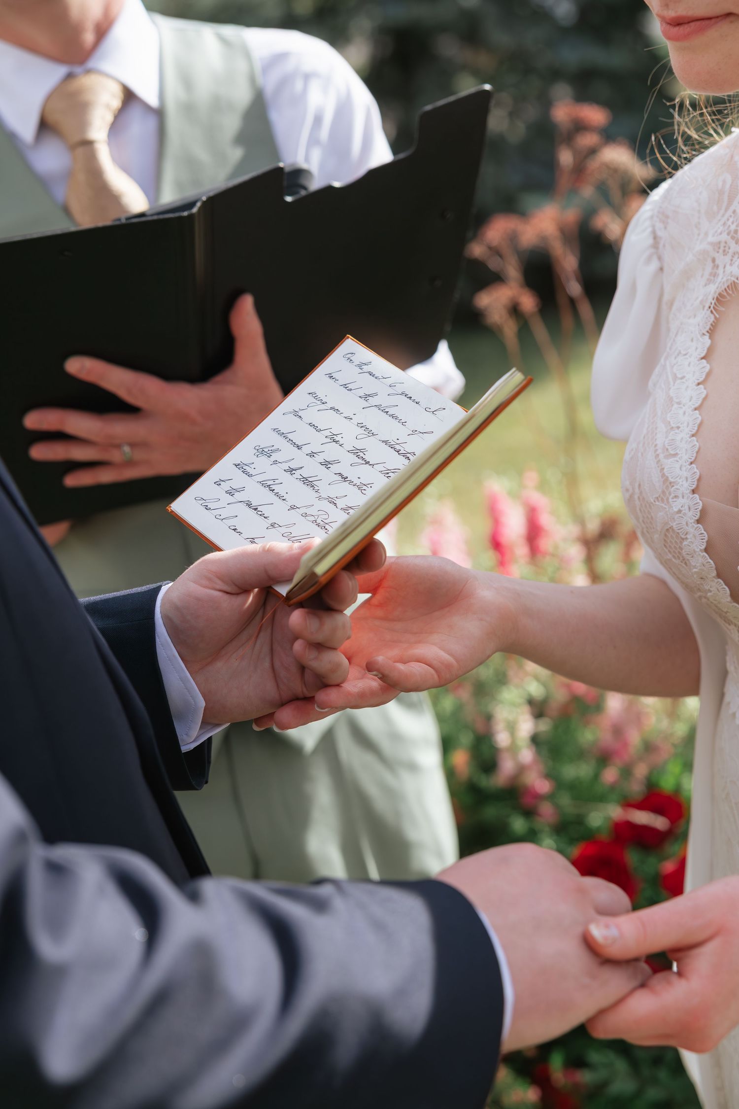 Close-up of bride and groom exchanging handwritten vows during outdoor wedding ceremony.