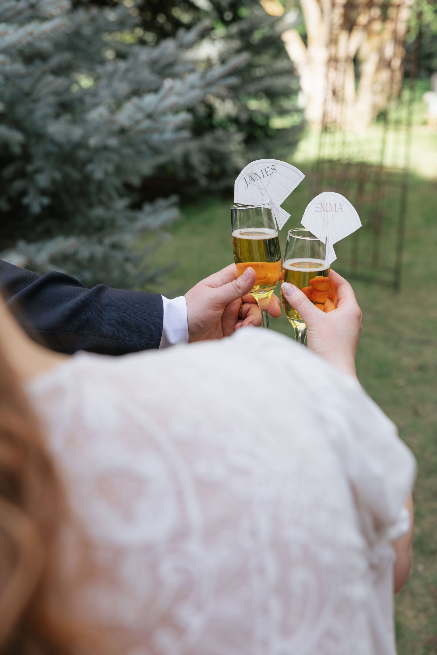 Bride and groom clink champagne glasses outdoors with personalized name tags at their wedding celebration.