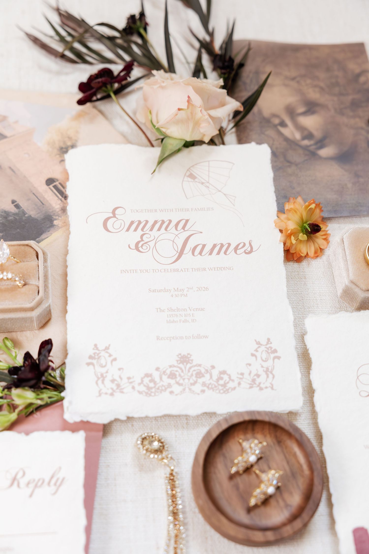 Wedding invitation for Emma and James displayed with flowers, jewelry, and reply card on white linen.