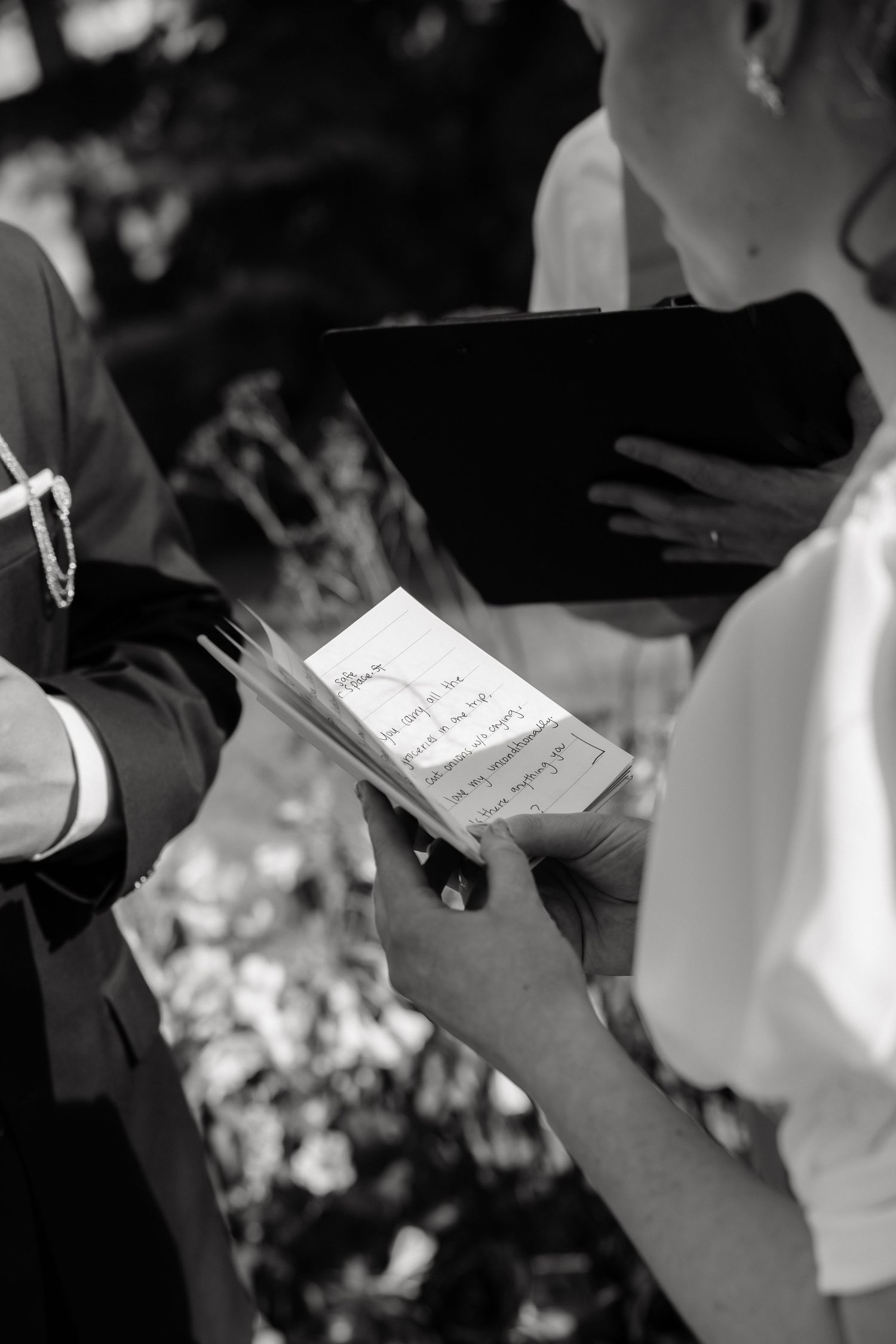 Black and white photo of a bride and groom exchanging handwritten wedding vows during an outdoor ceremony.