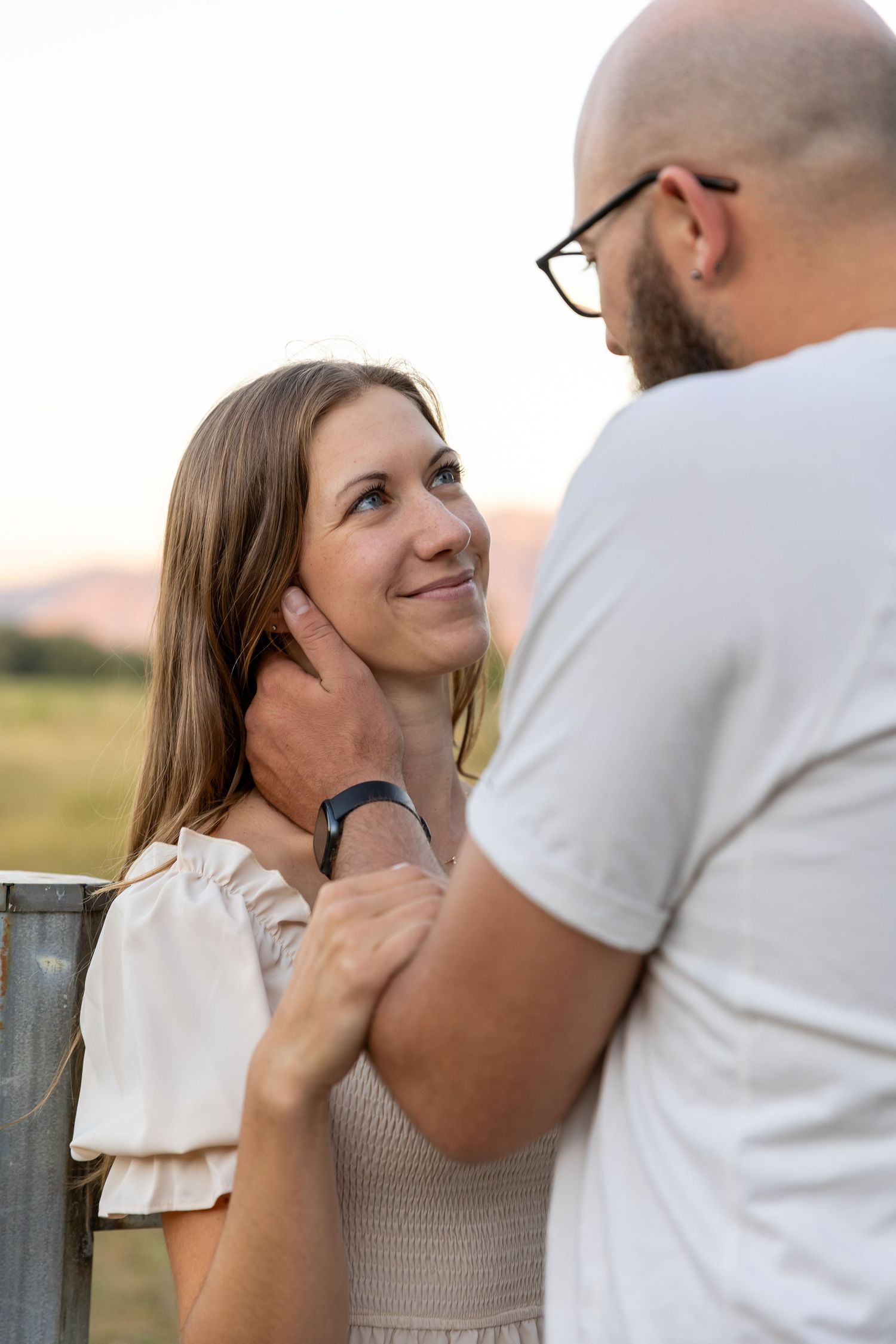 A couple shares a tender moment outdoors, man gently holding woman's face as she gazes up at him lovingly.