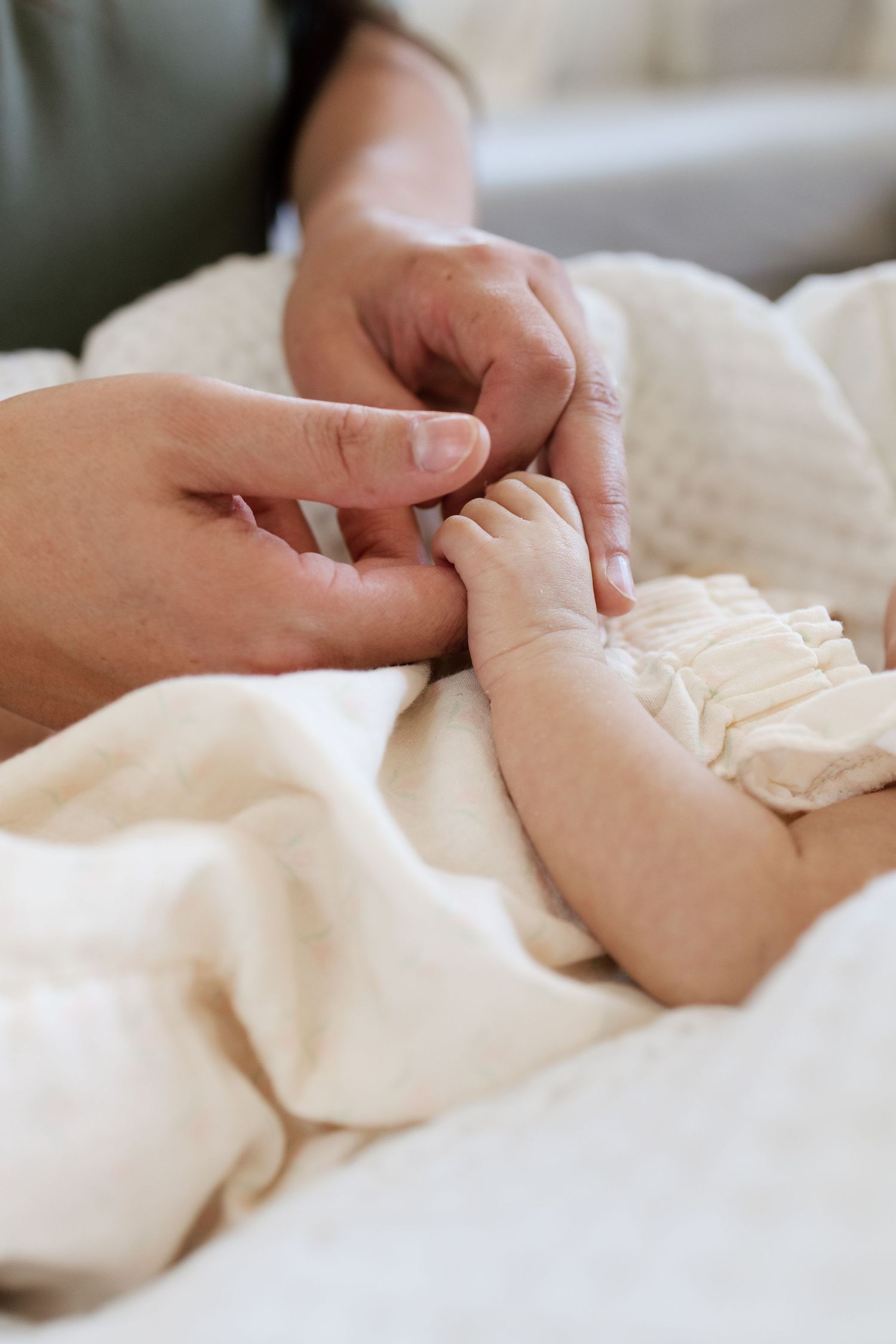 Close-up of an adult gently holding a newborn baby's tiny hand on a soft white blanket.