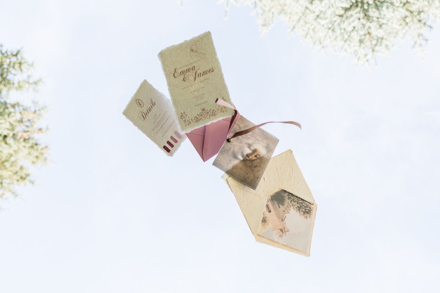 Elegant wedding invitation suite floating in the air with ribbon detail against a soft blue sky.
