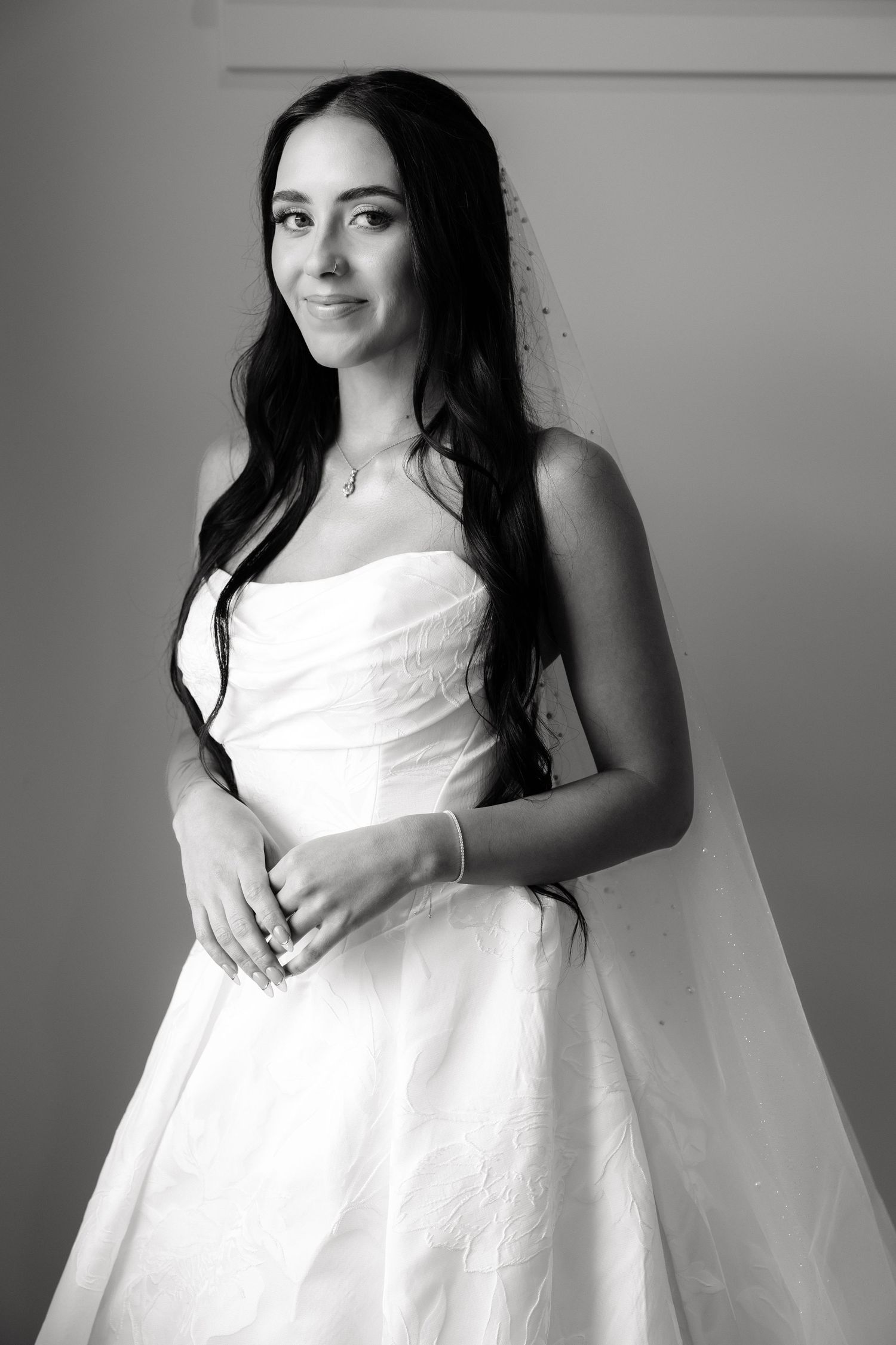 Black and white portrait of a smiling bride in a strapless gown and veil, with long dark hair.