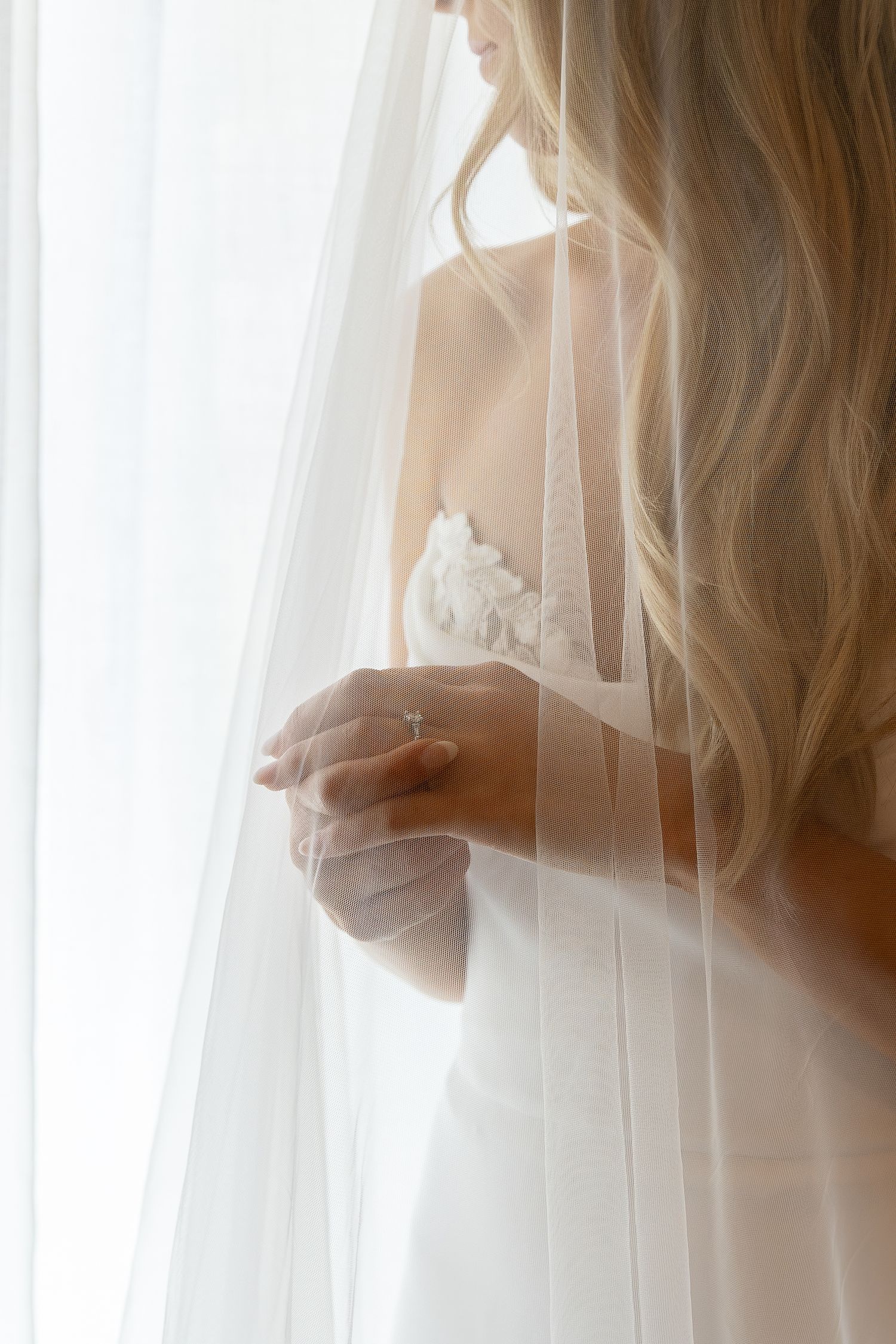 Soft, ethereal bridal portrait through sheer white curtains showing wedding dress details.