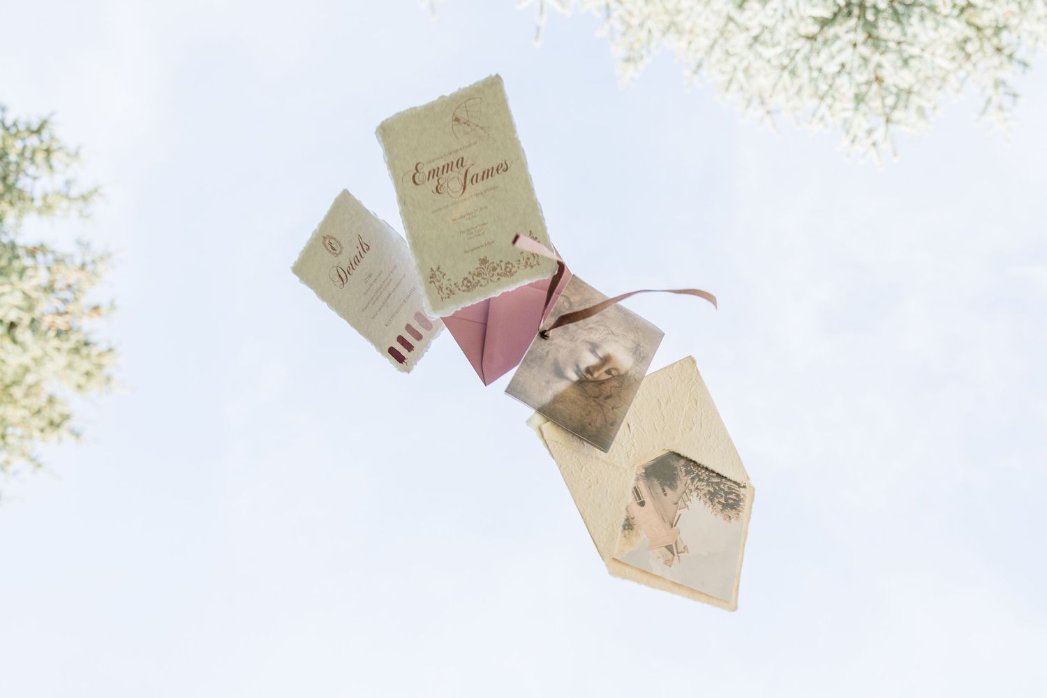 Elegant wedding invitation suite with envelope floating against a blue sky, surrounded by white flowers.