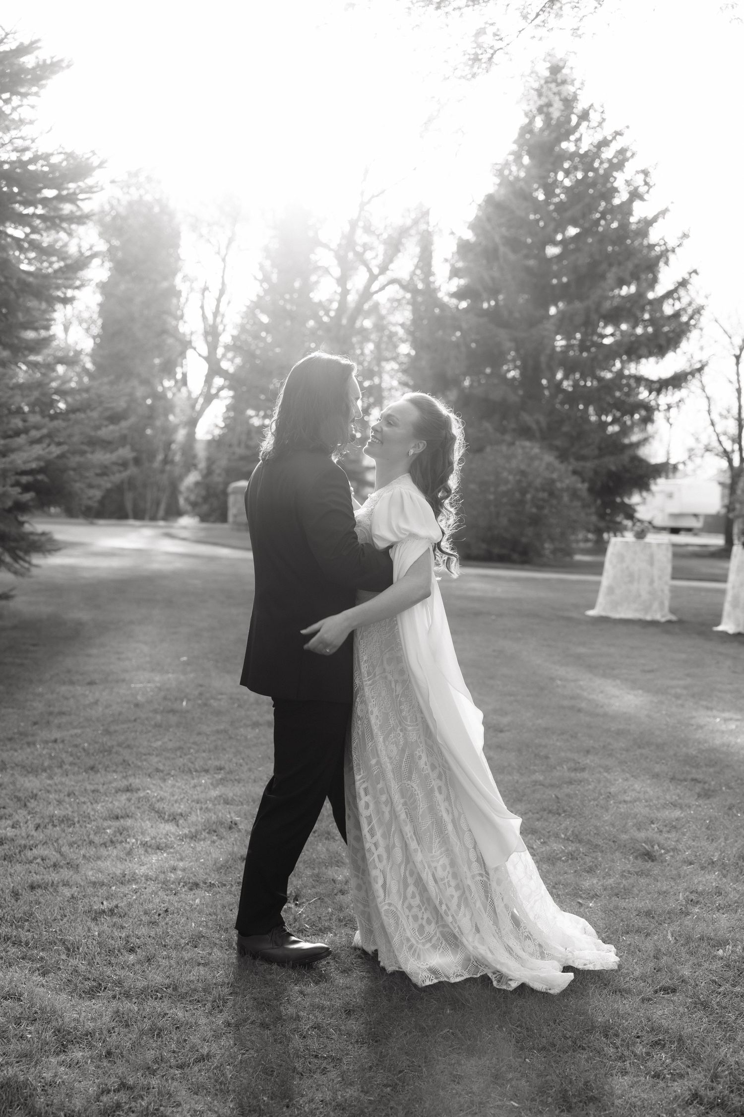 Black and white romantic photo of bride and groom embracing in a sunlit outdoor garden setting.
