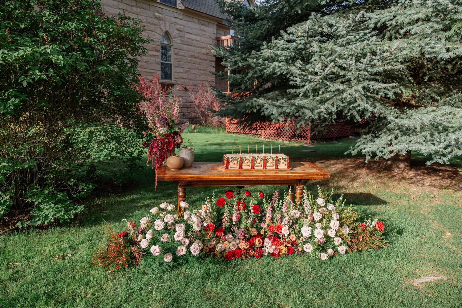 Rustic wooden table with floral ground arrangement of red and white blooms set in a lush garden wedding venue.