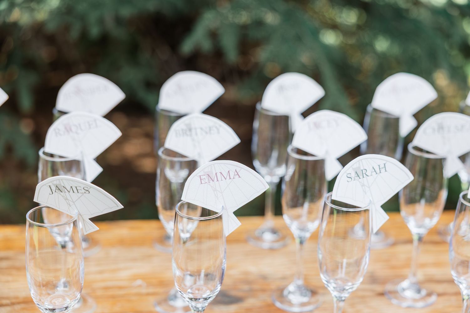 Elegant champagne flutes with personalized name cards for wedding guests, including Emma, Sarah, and James, displayed on a wooden table.