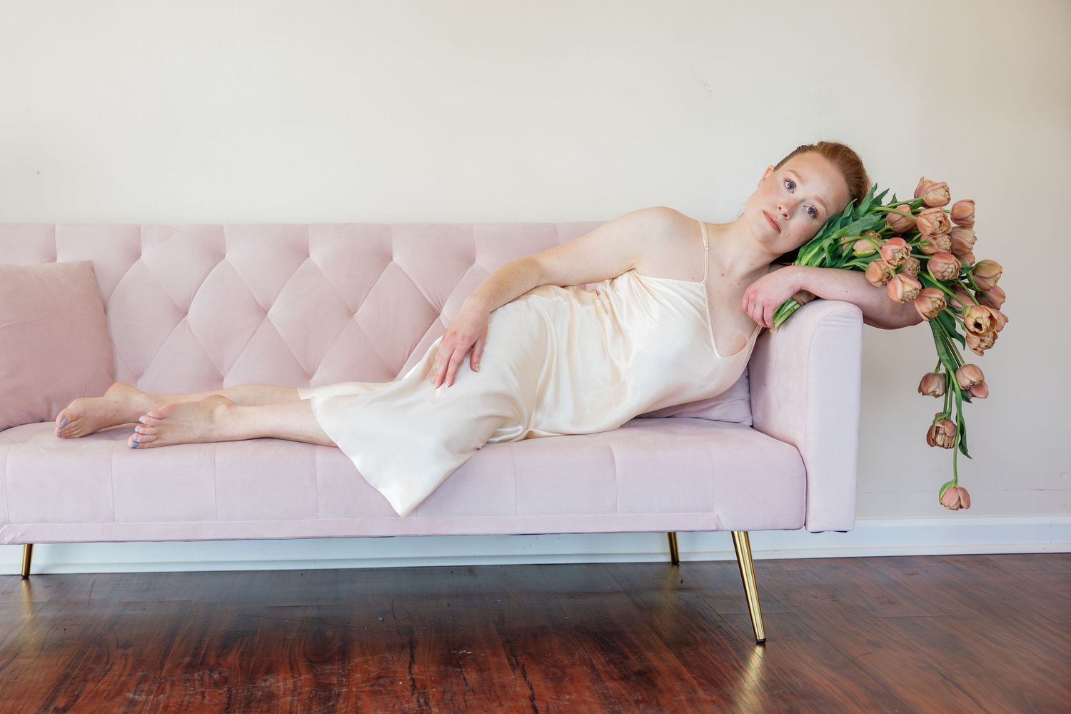 Bride in ivory dress reclining on pink velvet sofa with soft pink roses beside her.