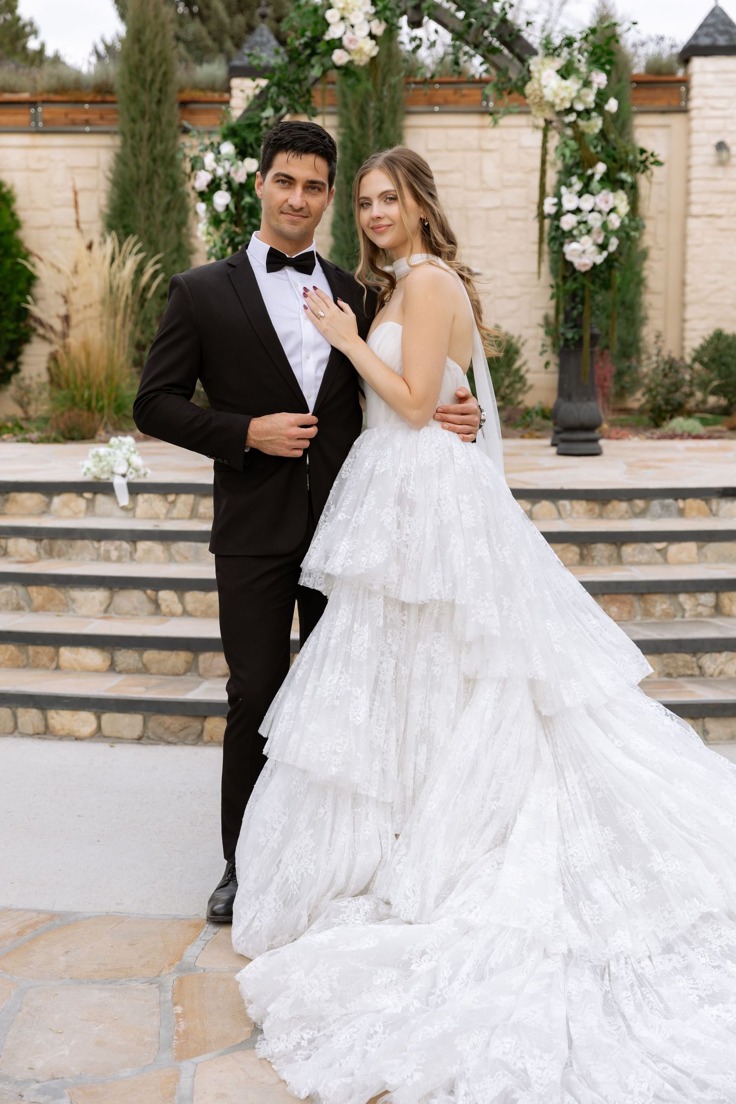 Wedding couple poses in front of elegant stone venue with flowing white gown.