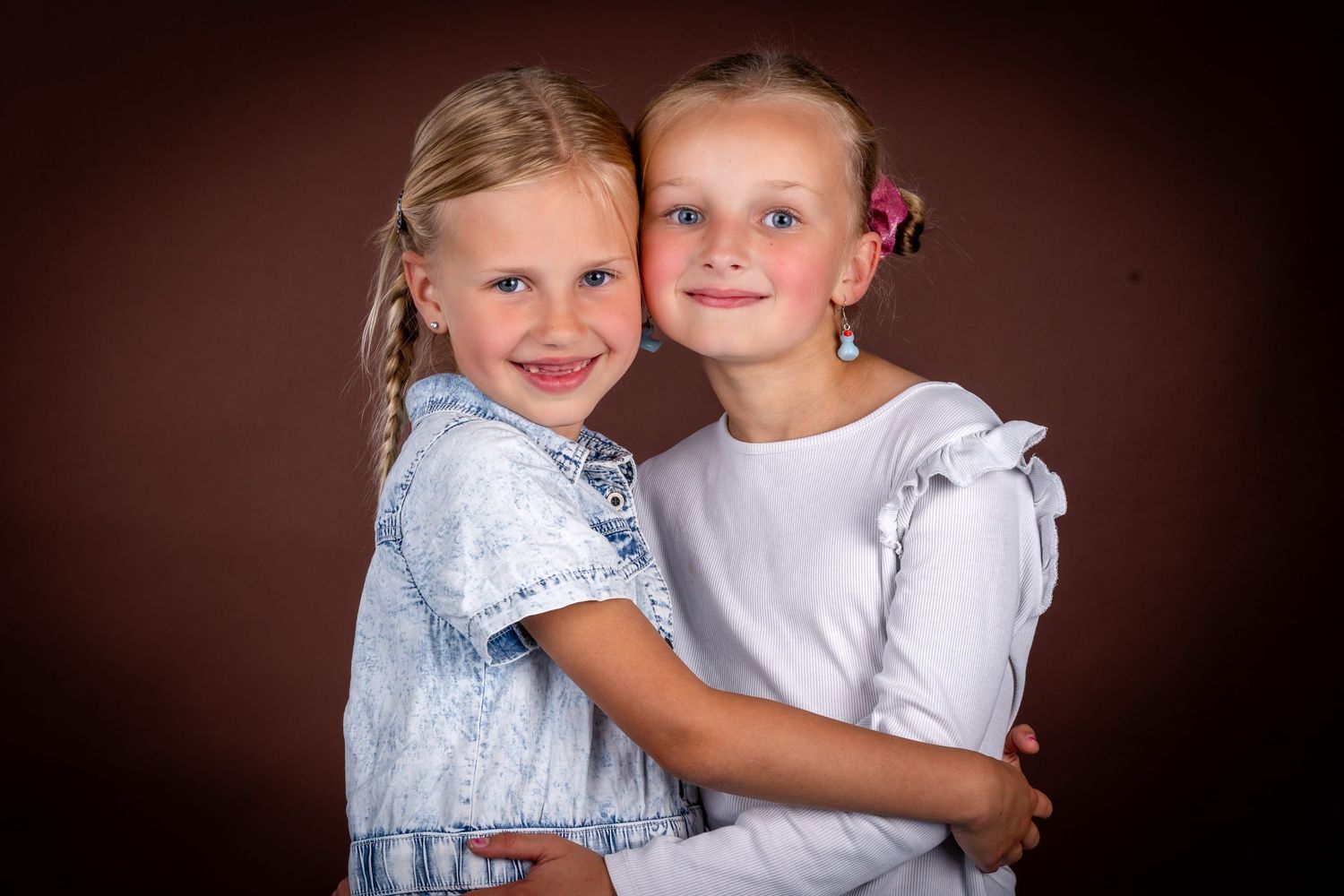 Two young children in white outfits pose together against a dark brown background in a series of candid photos.