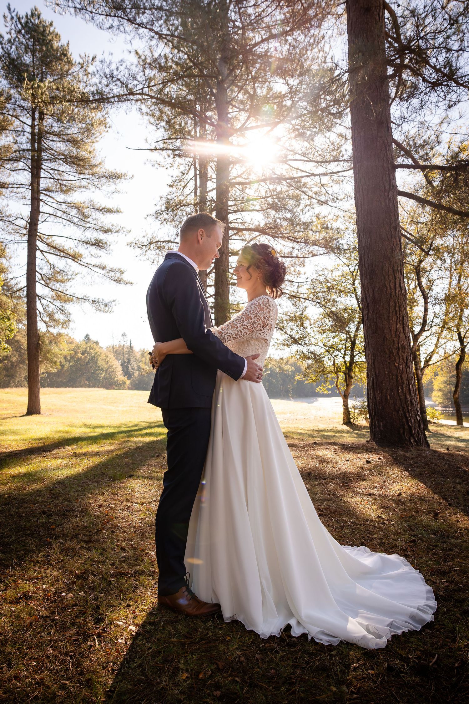 Sunlit forest wedding portraits with pine trees creating magical golden hour lighting.