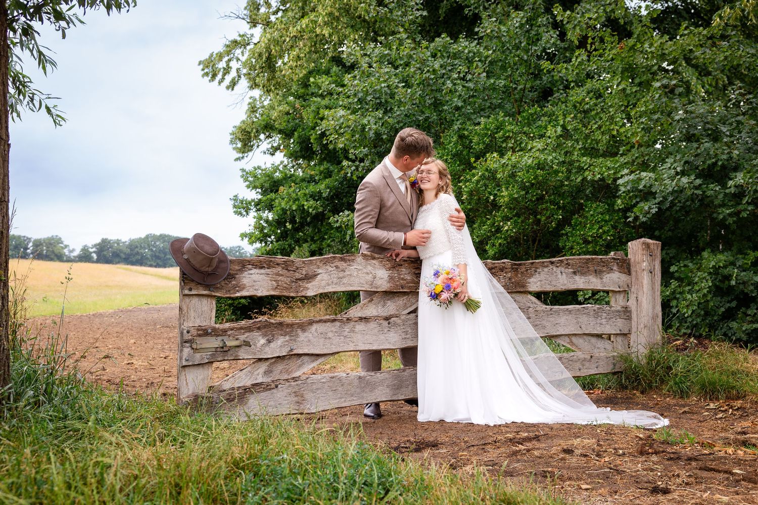 A romantic wedding portrait at a rustic wooden fence with flowing white veil.