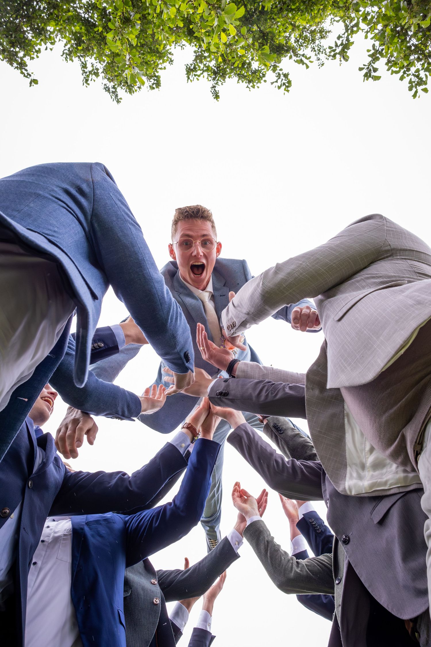 Low angle shot of groomsmen forming energetic huddle circle against white sky.