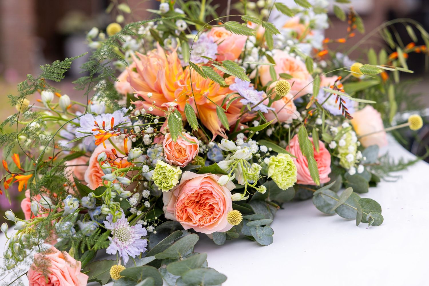 A romantic floral arrangement with peach roses, orange dahlias and delicate wildflowers.