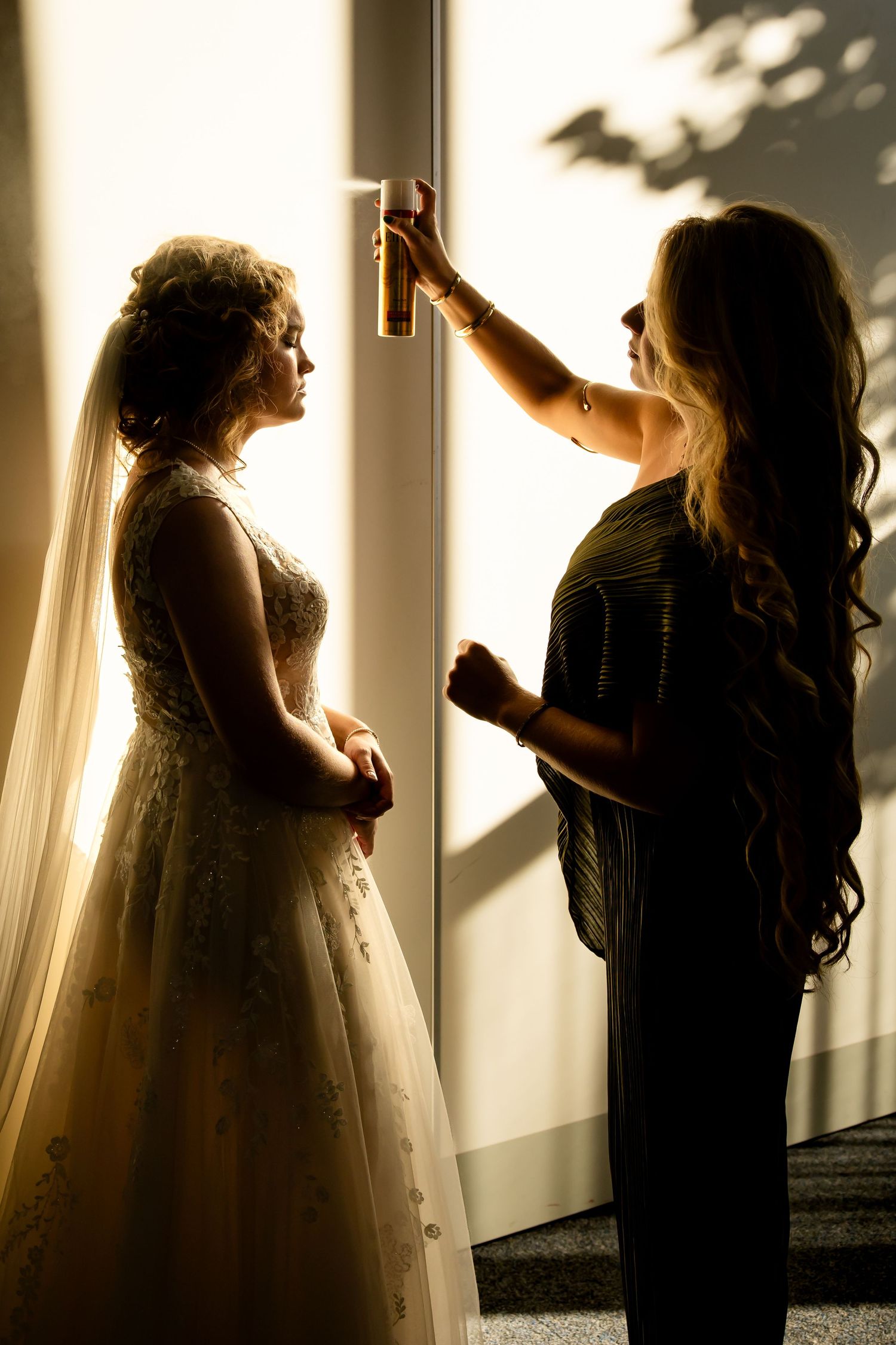 Silhouetted figures in wedding attire pose against bright window light creating dramatic shadows.