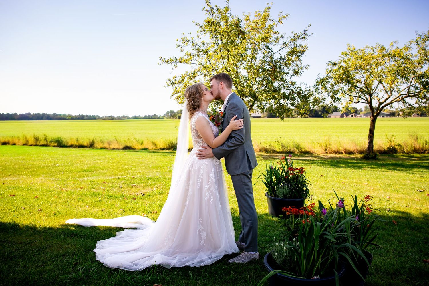 A romantic wedding kiss captured in a golden field during sunset with flowing veil and floral decorations.