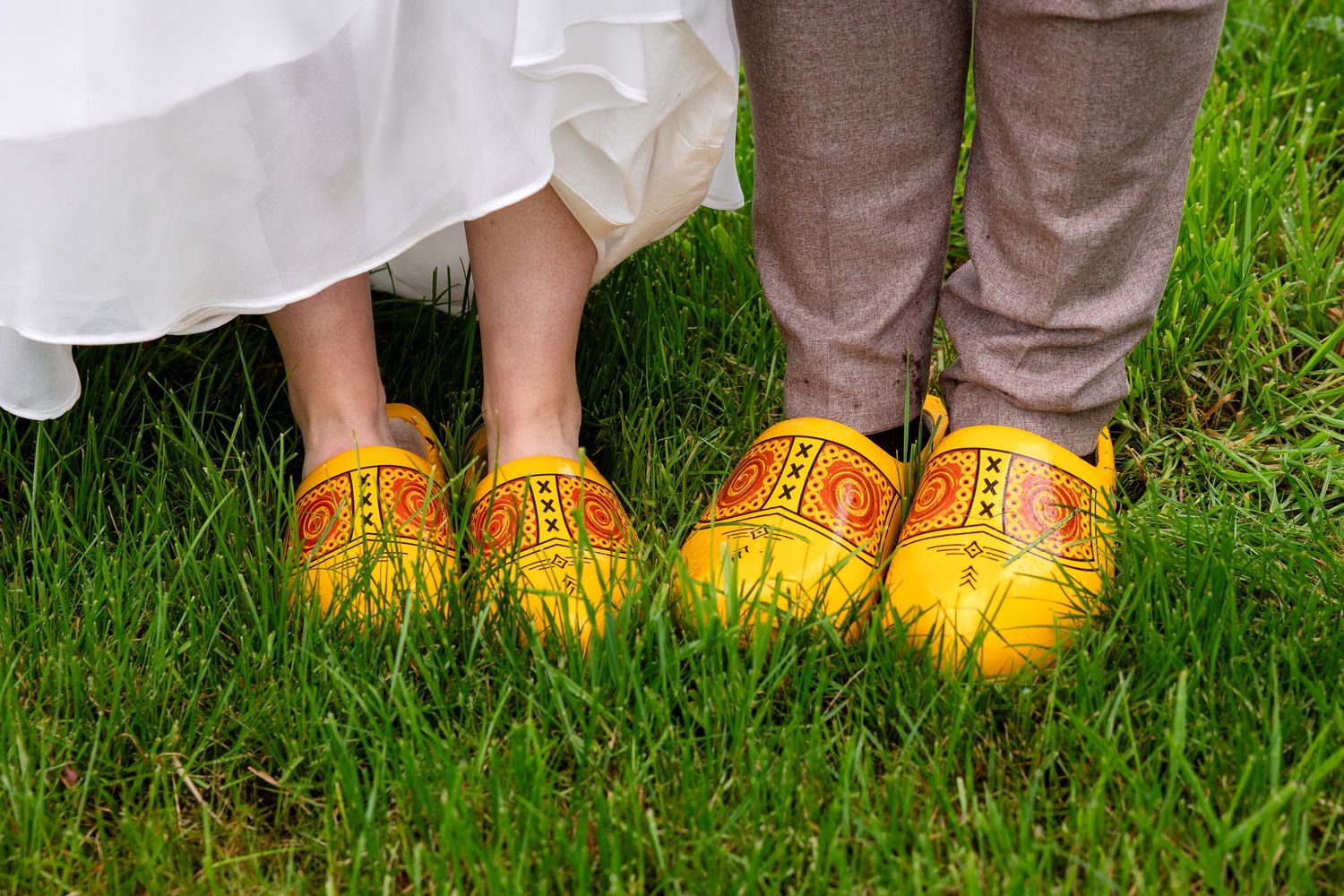 Two pairs of matching yellow wooden clogs worn on grass during a wedding photoshoot.
