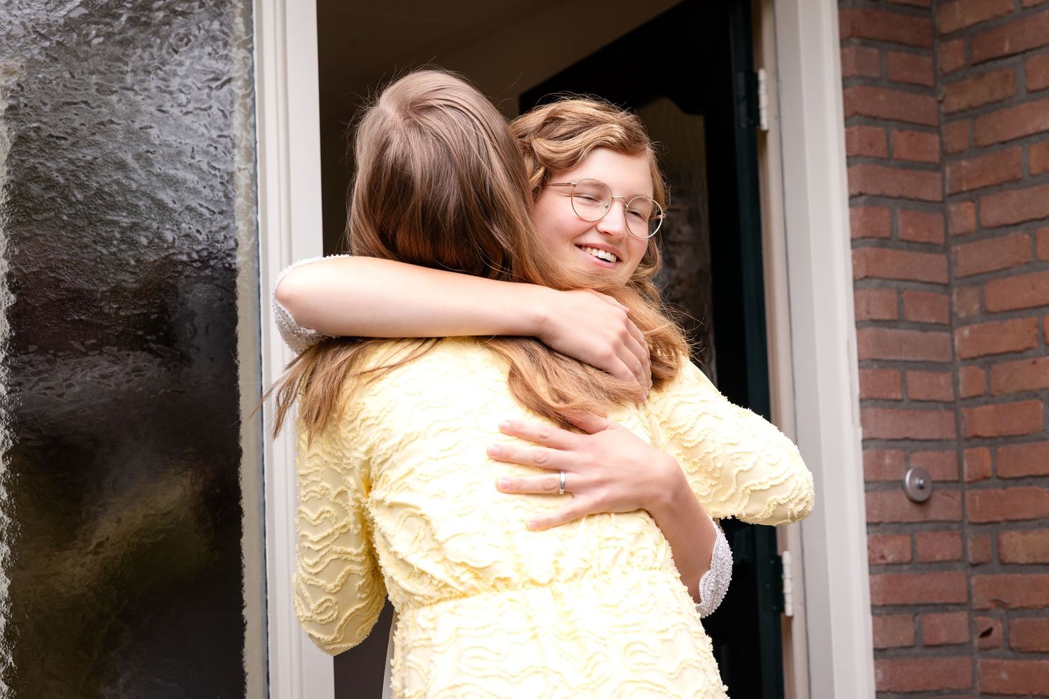 Two people share an emotional embrace in front of a brick wall.