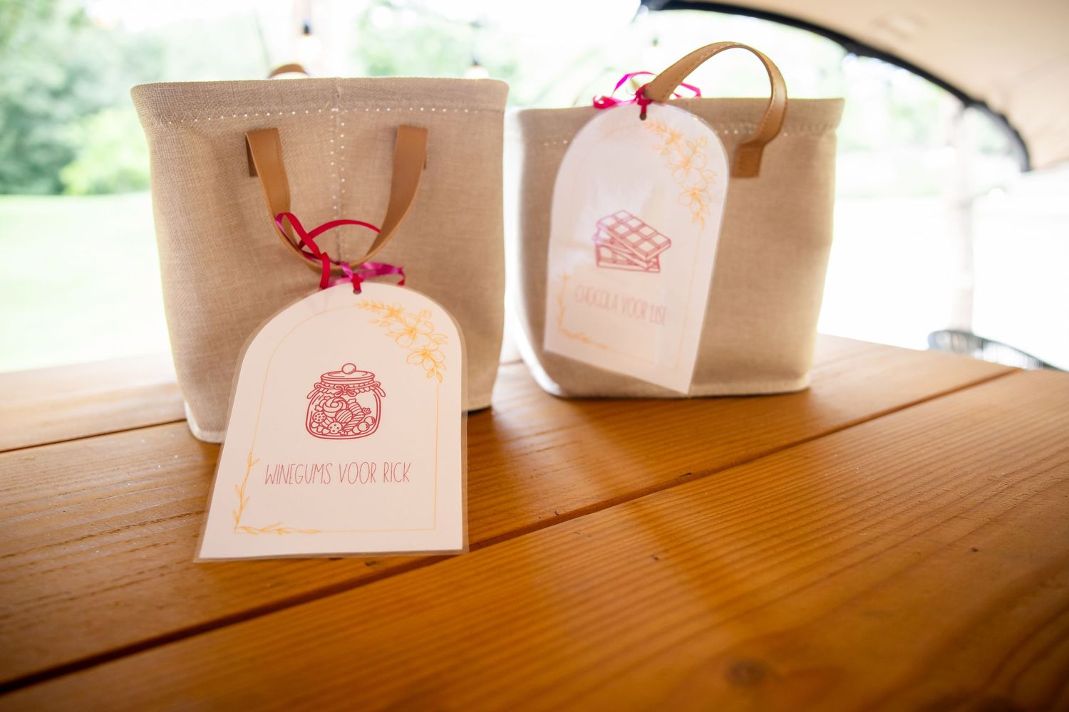 Twee elegante geschenkzakken met roze labels op een houten tafel tijdens de huwelijksreceptie.