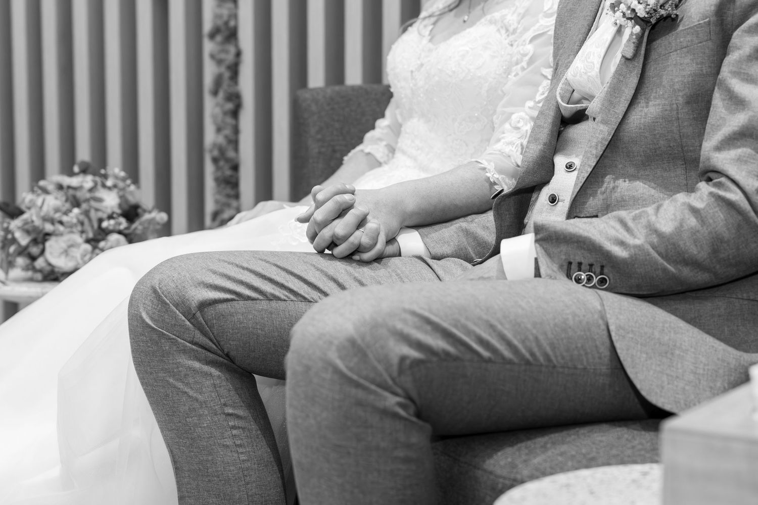 Black and white detail shot of couple sitting together during wedding ceremony.