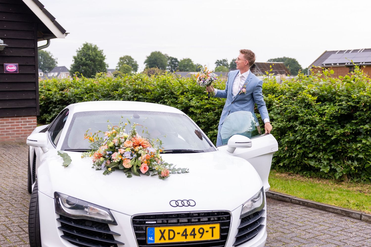 A white Audi R8 decorated with wedding flowers parked in front of a house.