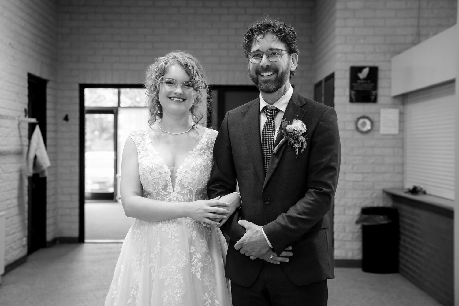 Black and white candid wedding moments captured in an indoor venue hallway.