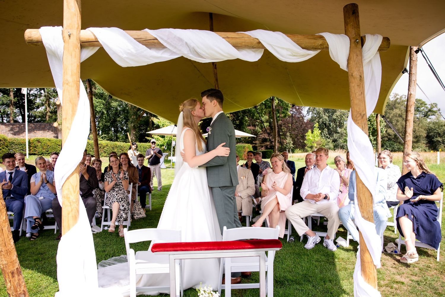 Bruiloftsreceptie in de buitenlucht onder witte tentversieringen, met gasten aan tafels.