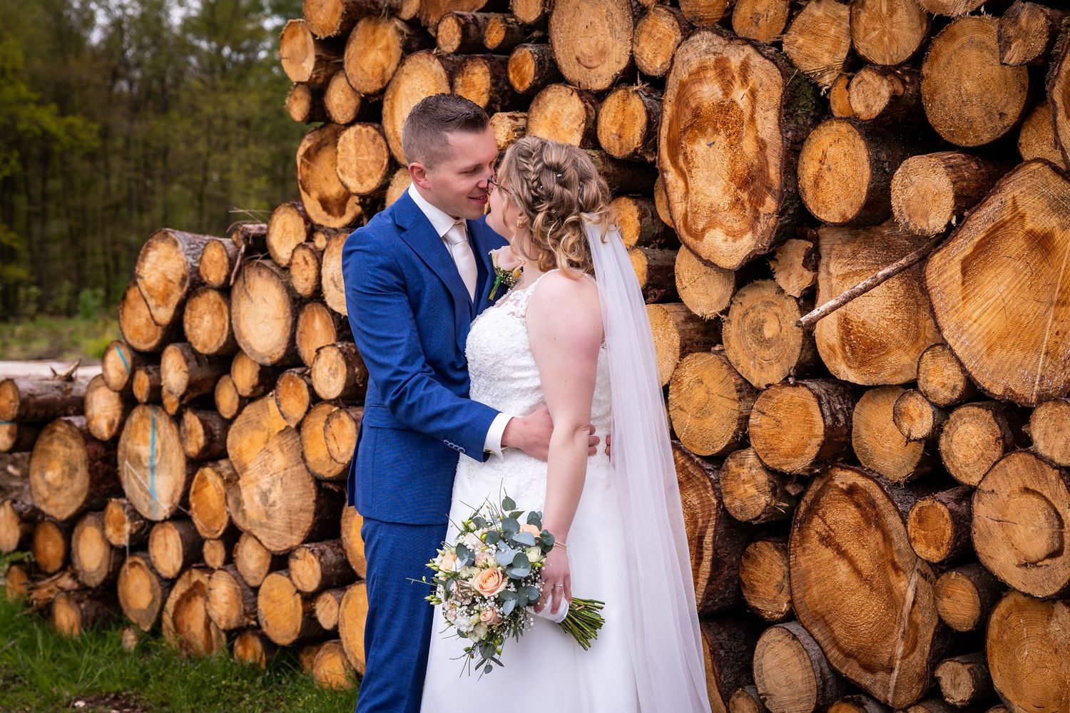 Romantic wedding photo shoot in front of stacked logs creating a rustic woodland backdrop.