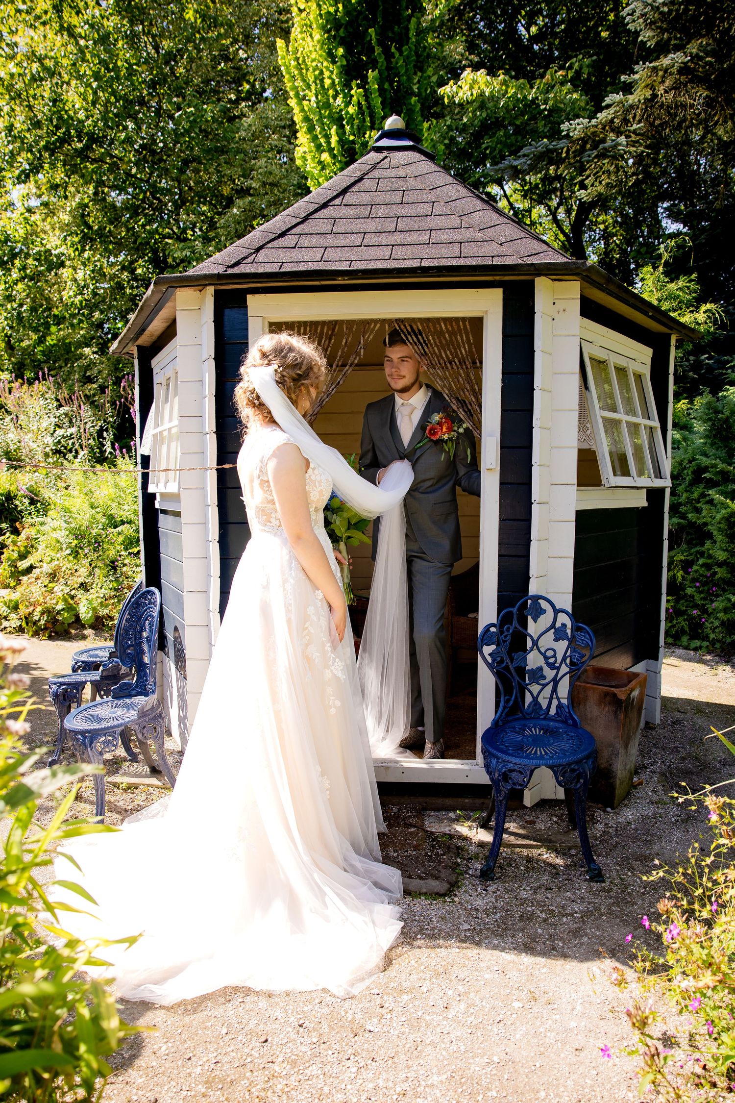 White garden gazebo decorated for wedding ceremony with blue chairs and gravel path.