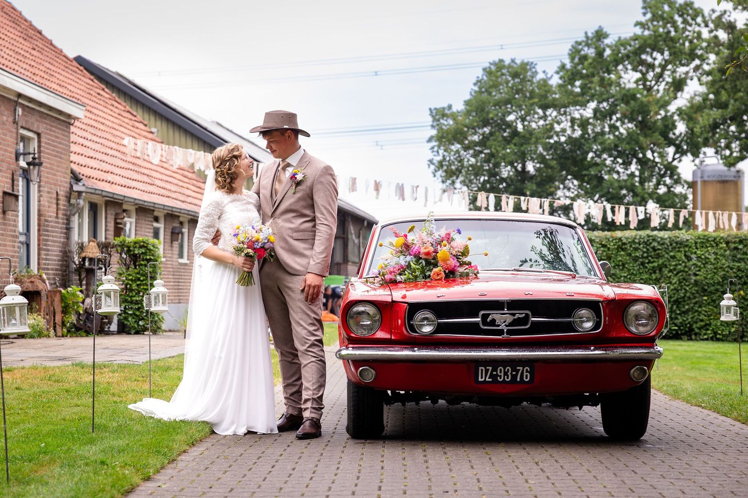 A vintage red Mustang parked near a brick house during a wedding celebration.