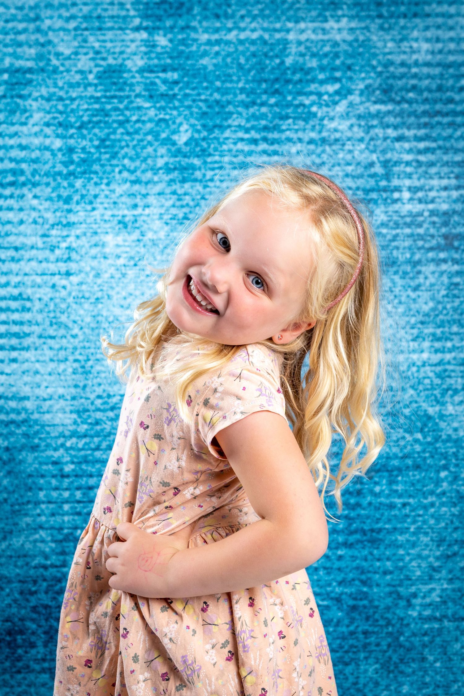 A young child with blonde hair wearing a floral dress twirls playfully against a bright blue textured background.